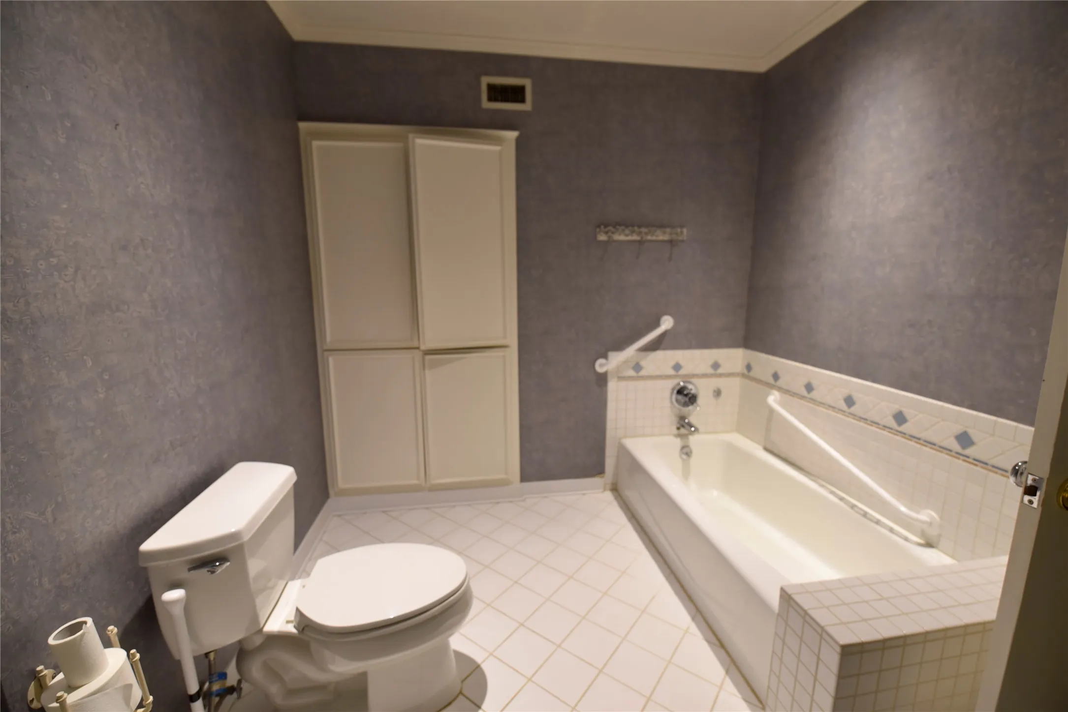 Full bathroom featuring a built-in tub with tile surround, white floor tiles laid in a diamond pattern, and a built-in storage cabinet with four panels