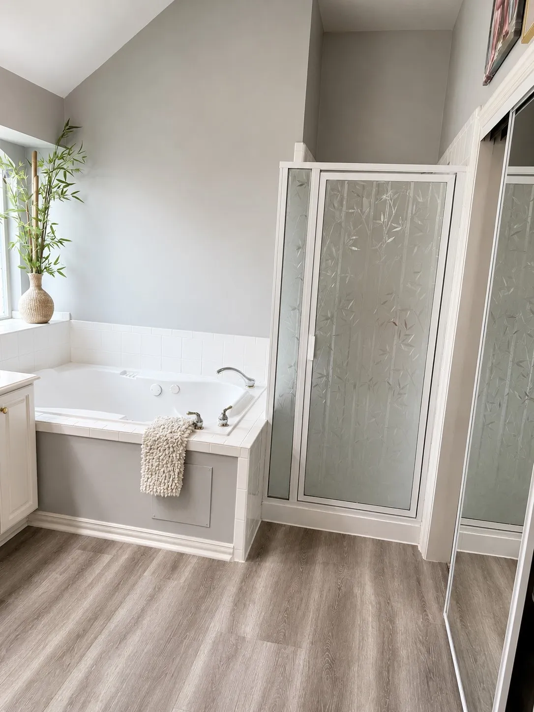Soaking tub with integrated jets, enclosed shower with patterned glass, wood-finish flooring, and vaulted ceiling