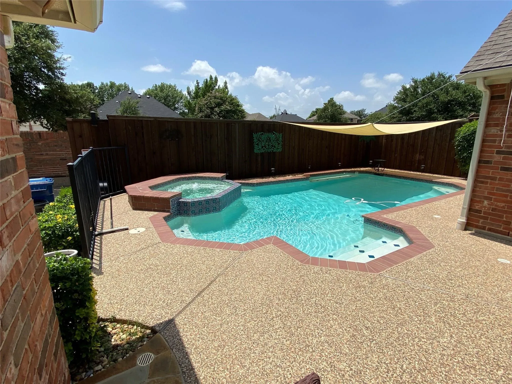 Backyard oasis featuring a swimming pool with integrated spa, expansive aggregate patio, and privacy fencing