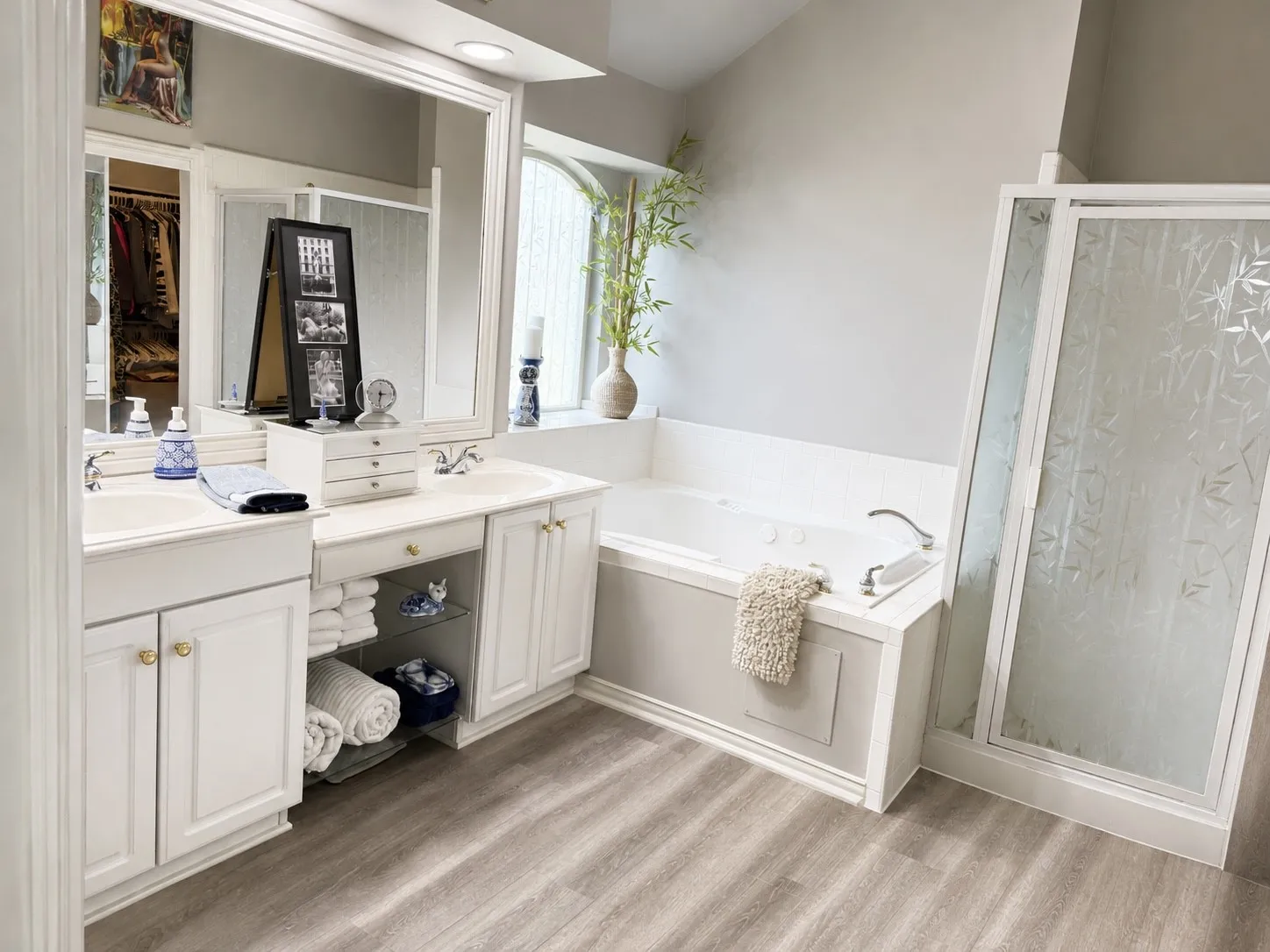 Dual vanity with integrated sinks, built-in bathtub, separate shower enclosure with frosted glass, and wood-finish flooring
