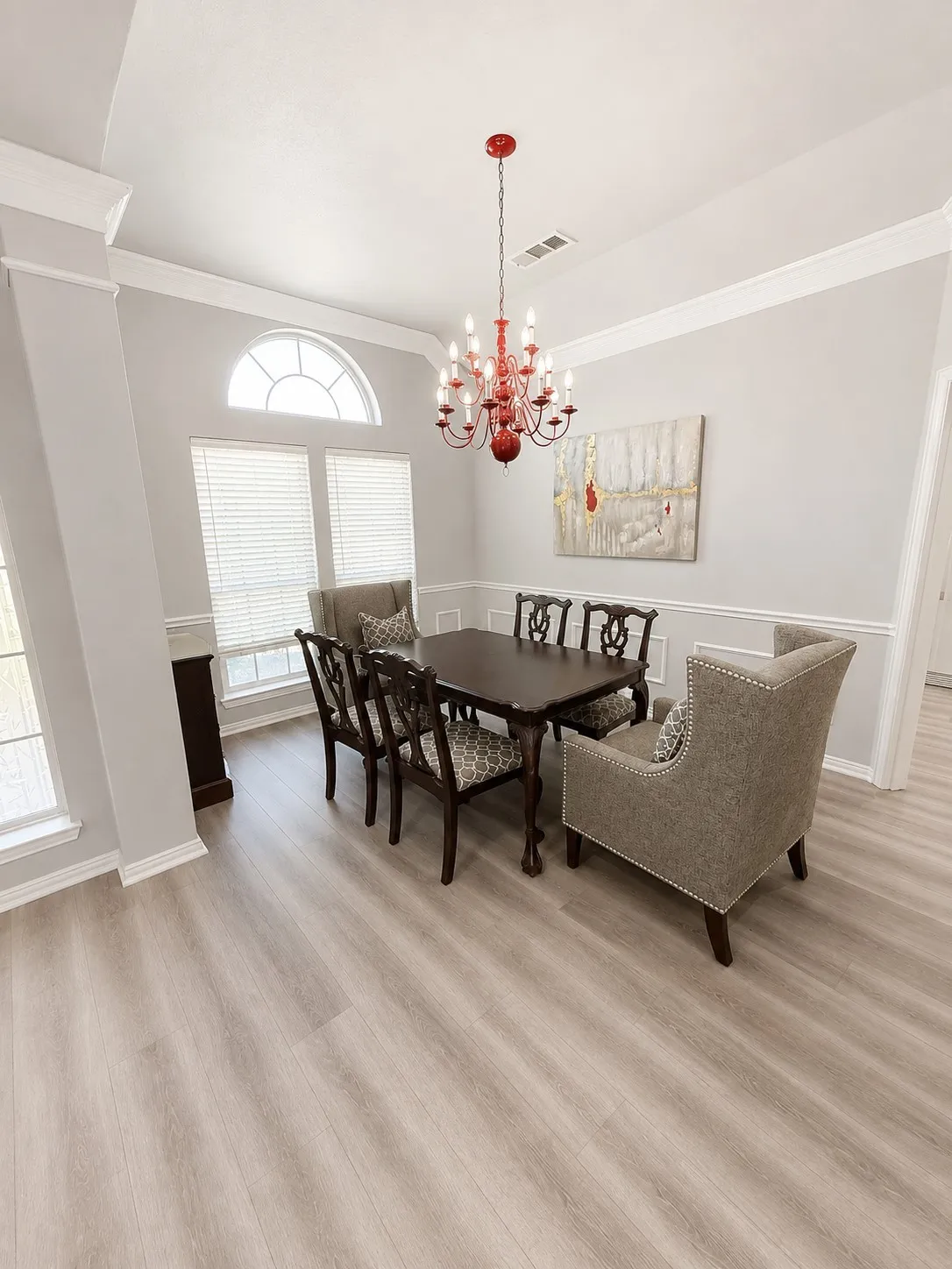 Elegant dining room featuring hardwood-finish flooring, crisp white walls with chair rail molding, and abundant natural light from multi-pane windows with transom detail
