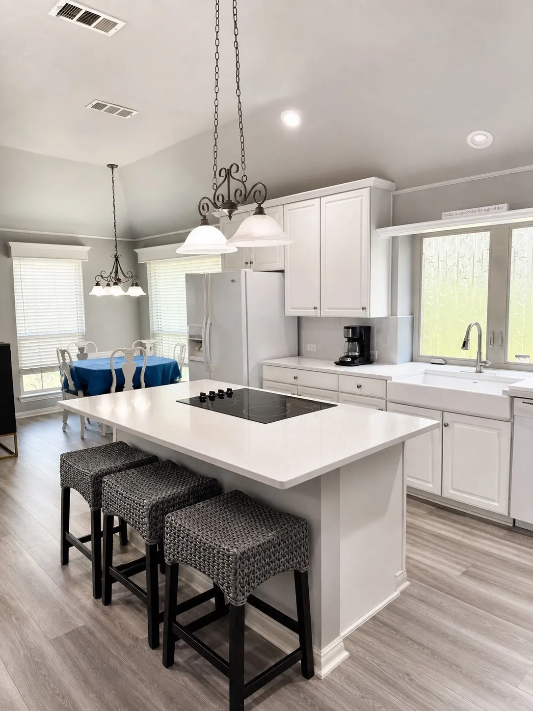 Kitchen with vaulted ceiling, white cabinetry, a center island with an integrated cooktop, a farmhouse sink, and wood-finish flooring