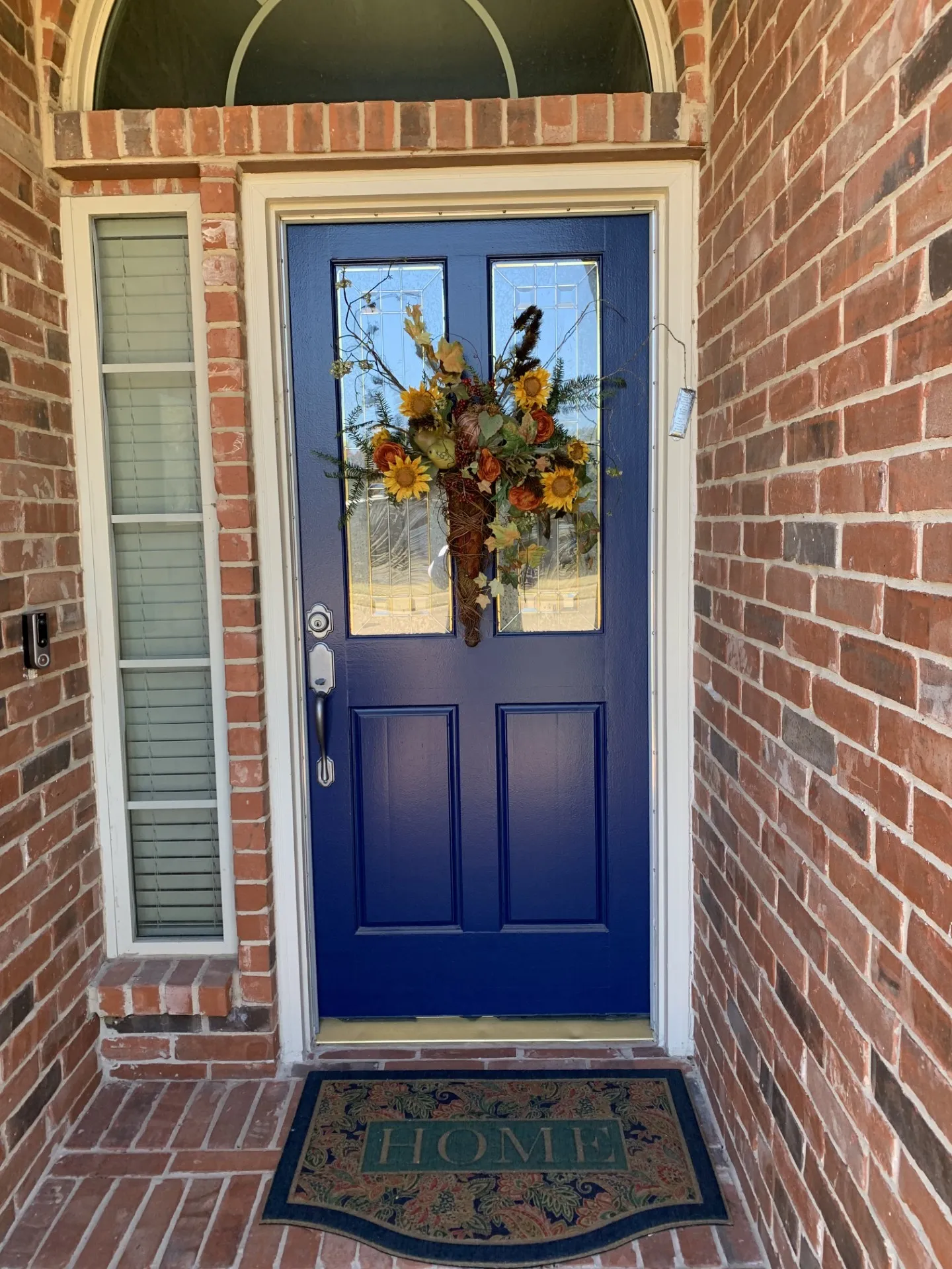 Brick exterior featuring a vibrant blue front door with upper glass panels, an arched transom window, and a vertical sidelight with blinds