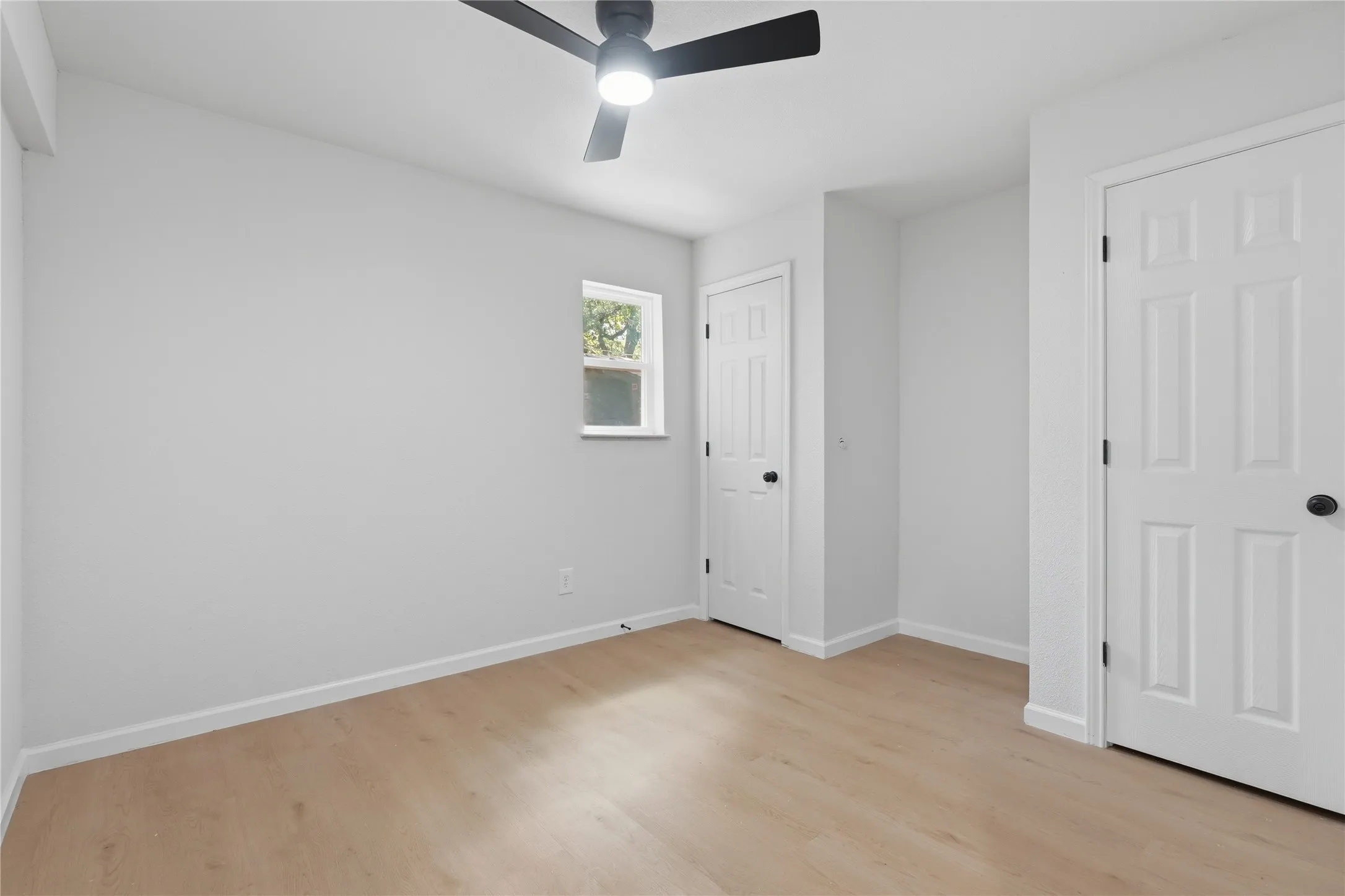 Light-filled room featuring wood-finish flooring, white walls, and a contemporary ceiling fan