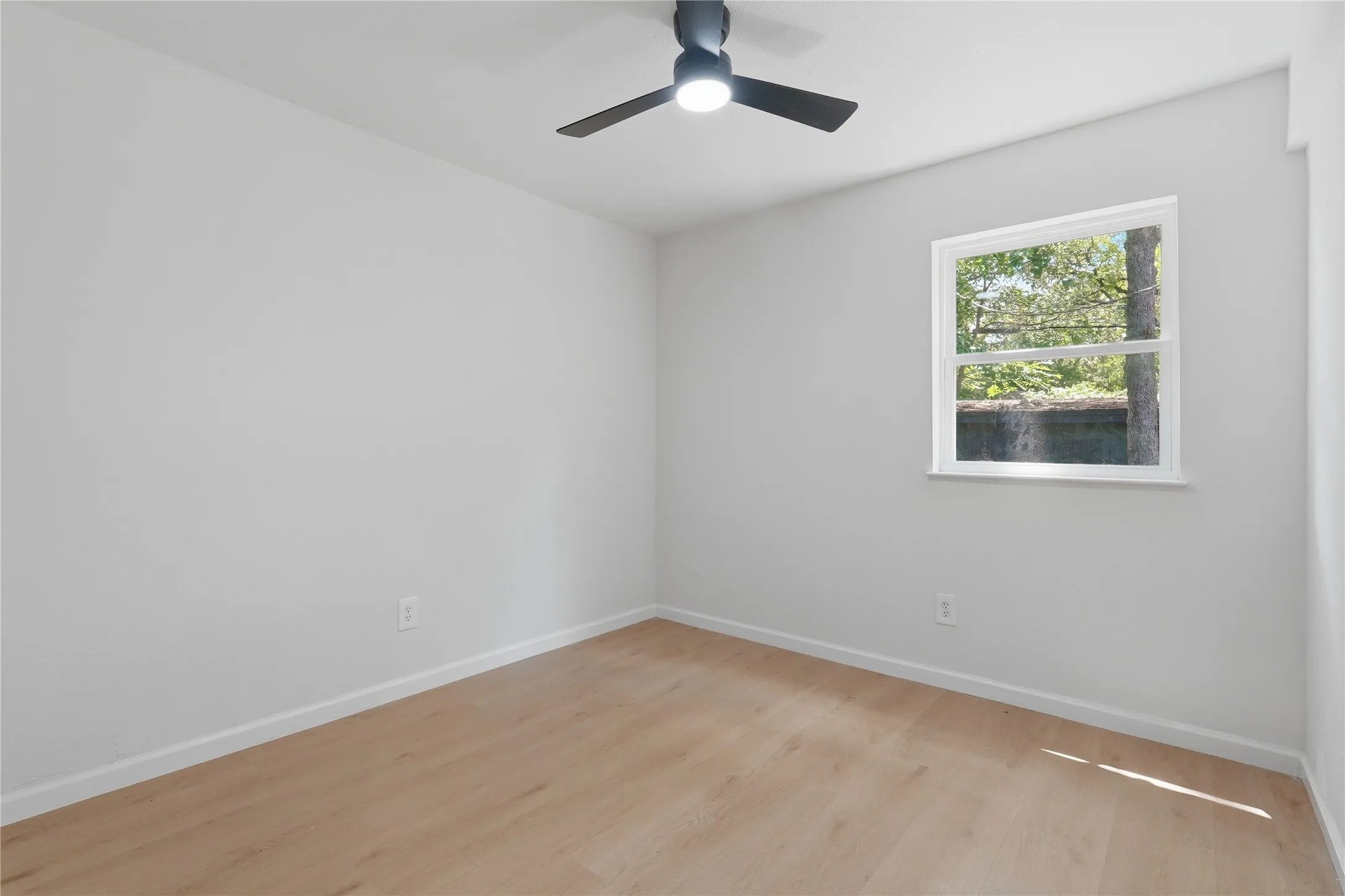 Light-filled room featuring wood-finish flooring, white walls, and a modern ceiling fan with integrated lighting