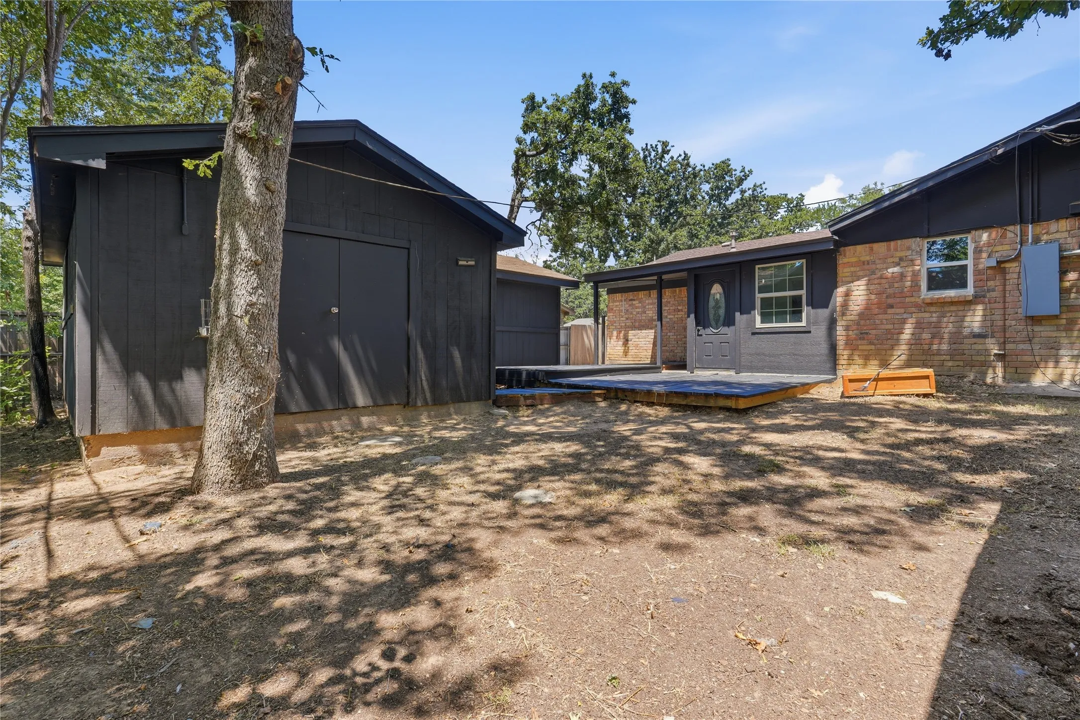Expansive yard featuring a large detached shed with double doors and a covered patio area with wood decking