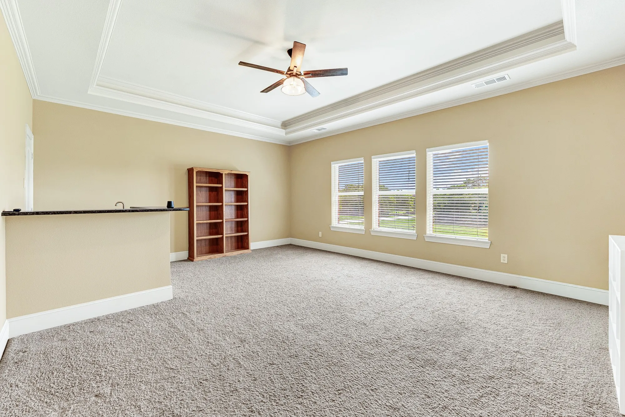 Three large windows draw natural light across the expansive carpeting, illuminating a deep tray ceiling with elegant crown molding. Imagine setting up a billiards table under the ceiling fan for a relaxed weekend tournament with friends.