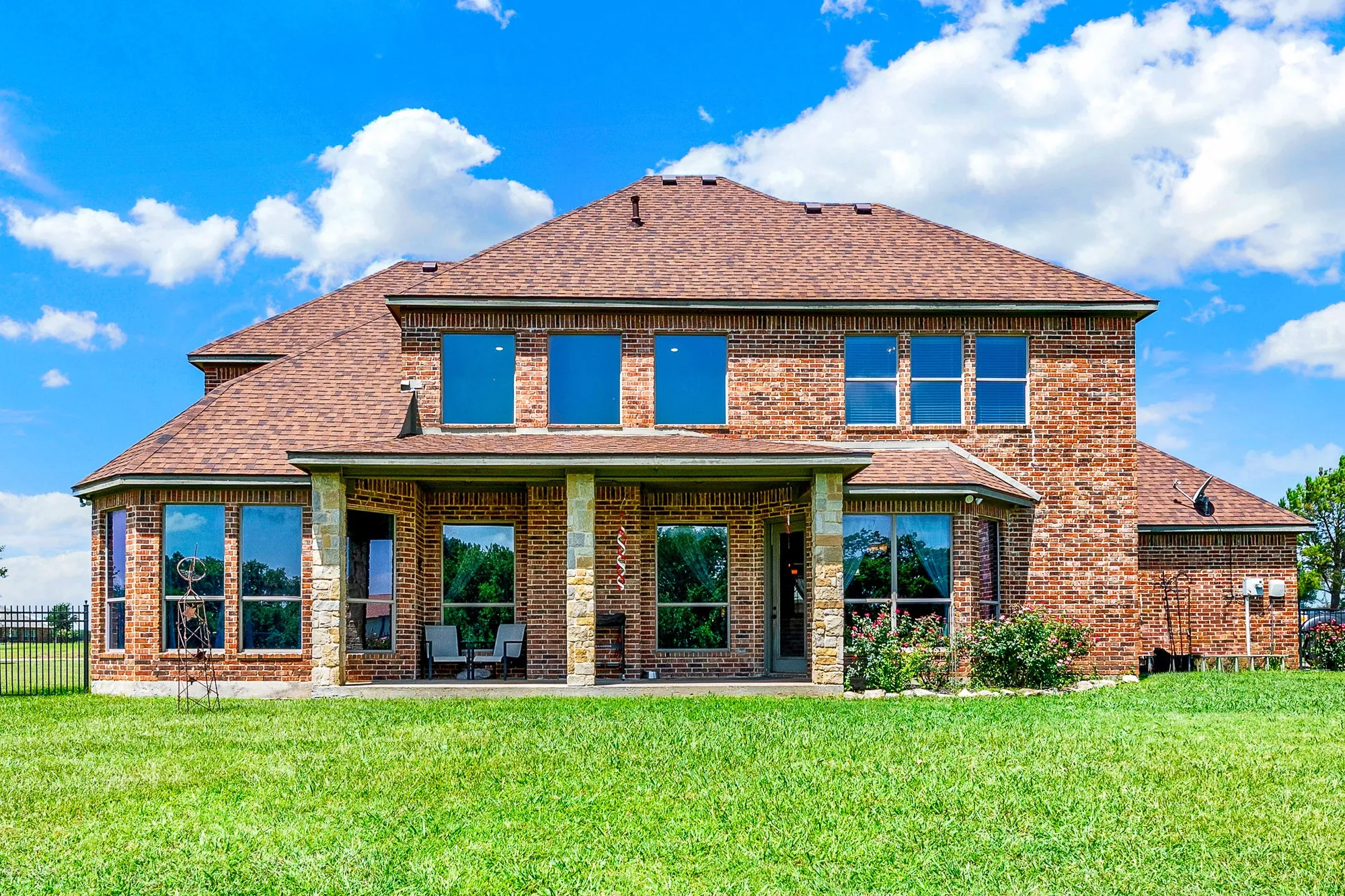 A deep covered patio stands supported by sturdy stone pillars, framing a massive array of rear windows that draw the afternoon light inside. You will love hosting lively summer barbecues here, staying cool in the shade while keeping an eye on the lawn.