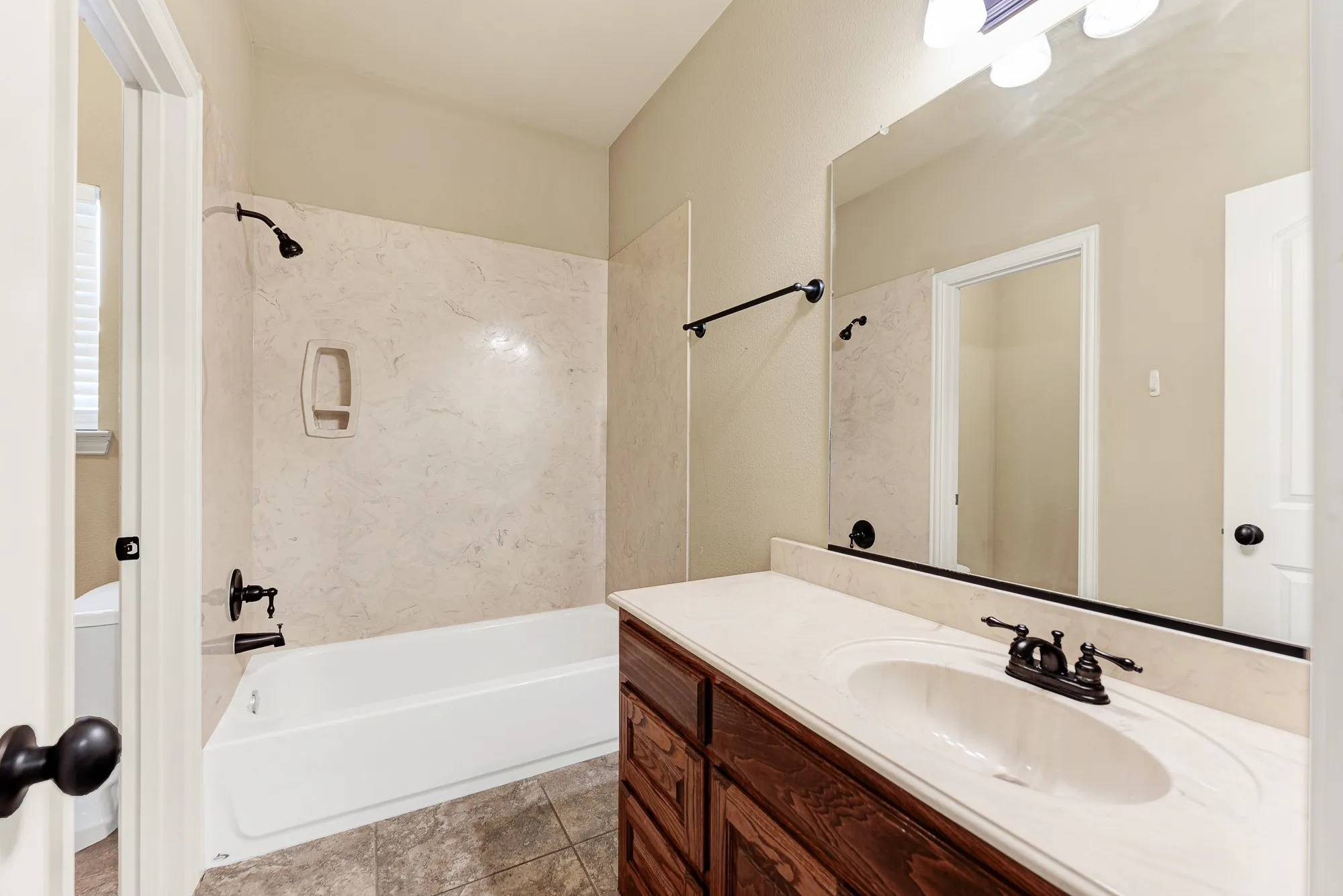 A wide vanity mirror catches the warm overhead glow, expanding the visual depth of the neutral tile flooring and structured cabinetry. Guests will love having a dedicated, well-lit station to comfortably unpack their essentials and ease into their evening routine.