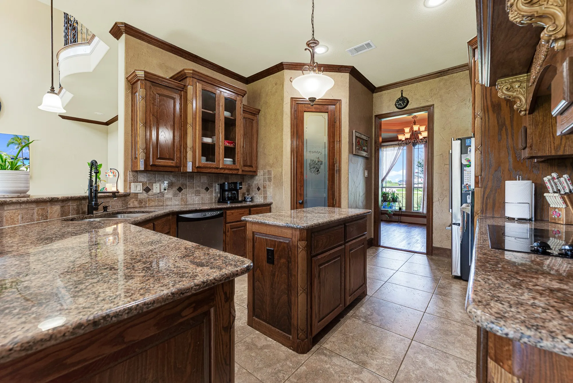 Multi-level granite countertops capture the light, framing a clear sightline toward the frosted glass pantry door. It is a natural hub where friends can lean against the bar and chat while you put the finishing touches on dessert.