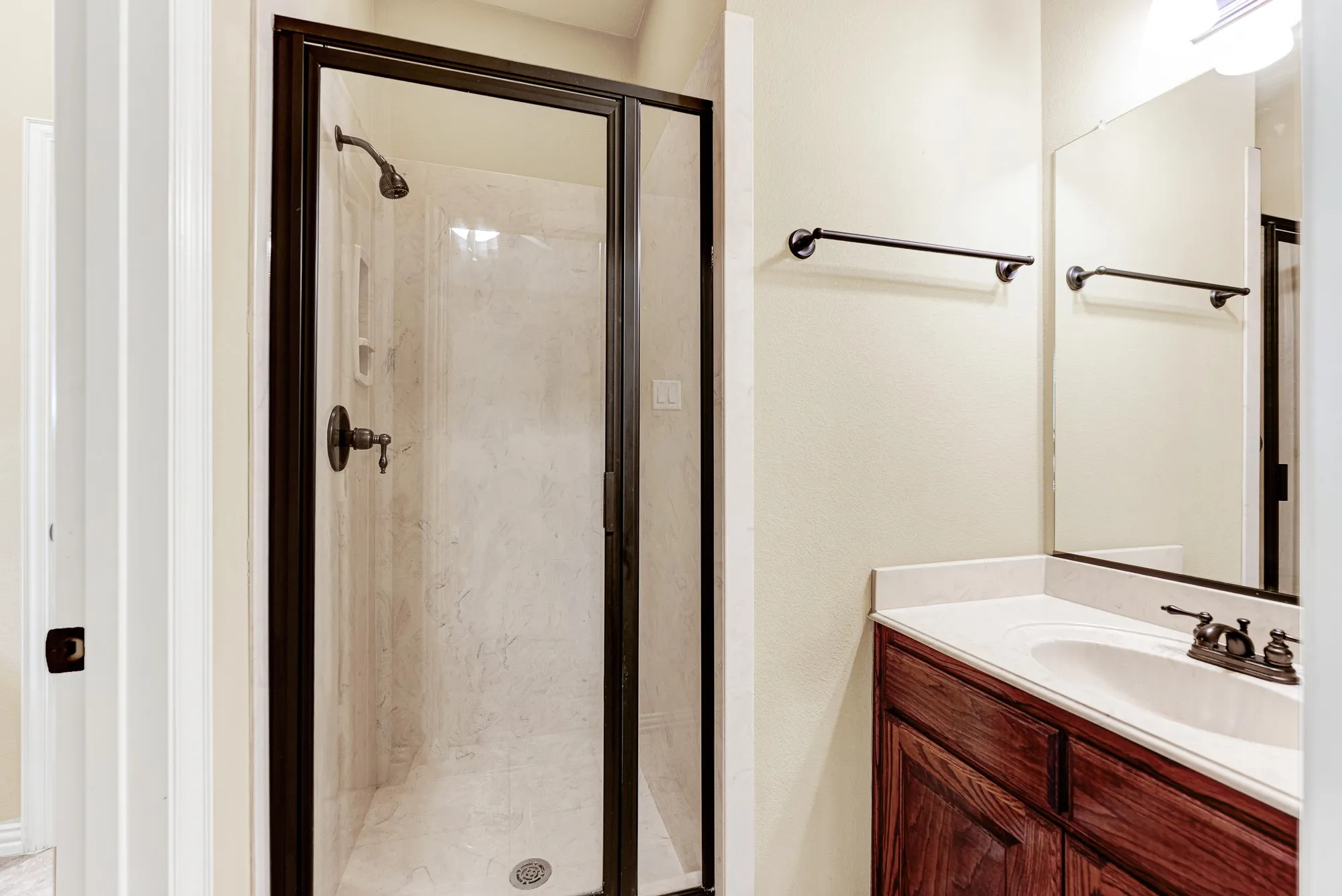 A crisp glass-framed walk-in shower features light tile surrounds that reflect the vanity's bright overhead illumination. Visitors will love the refreshing feel of this bright space as they prepare for a morning out.