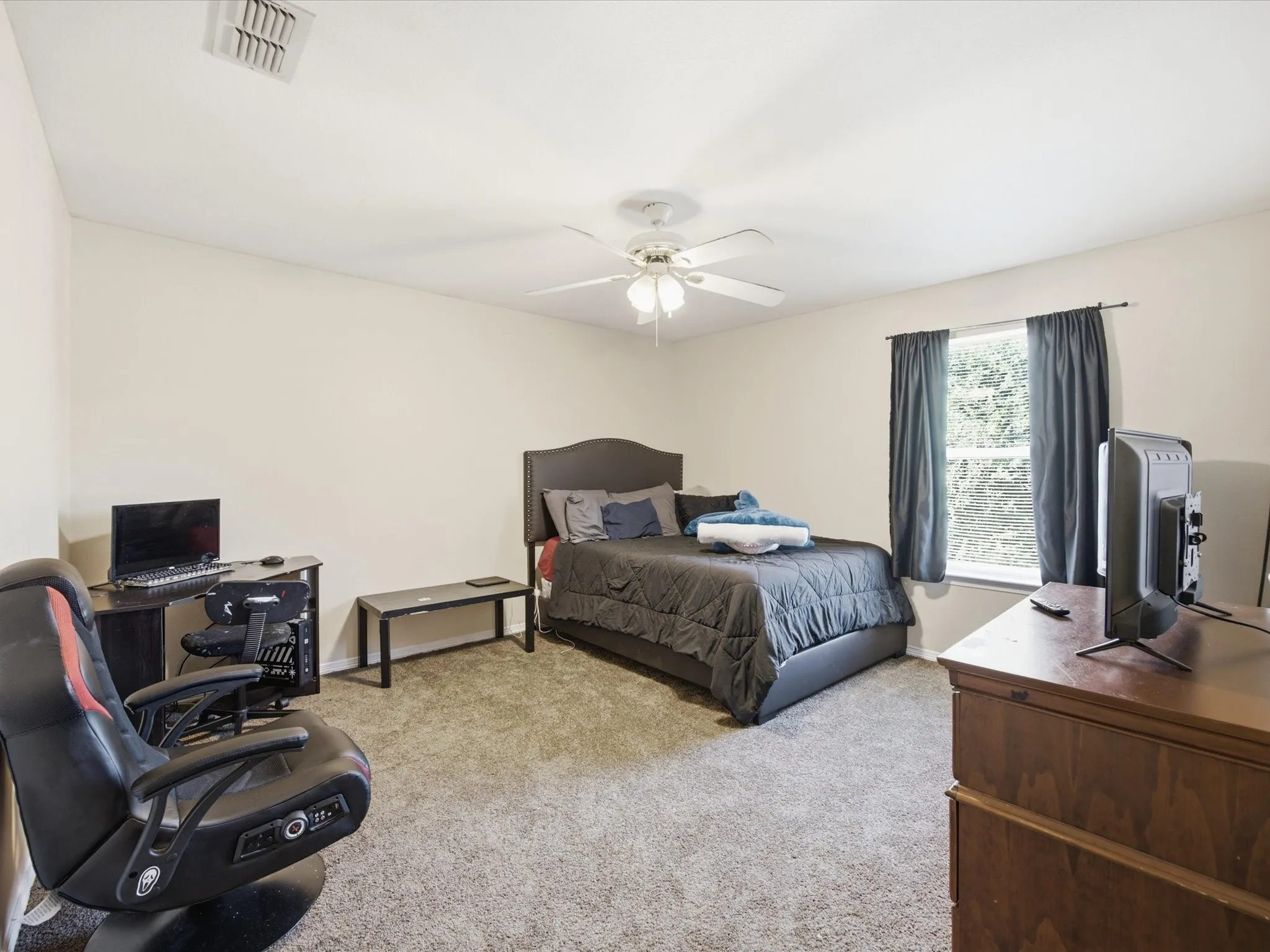 Carpeted room featuring light-toned walls, a window with dark curtains, and a ceiling fan