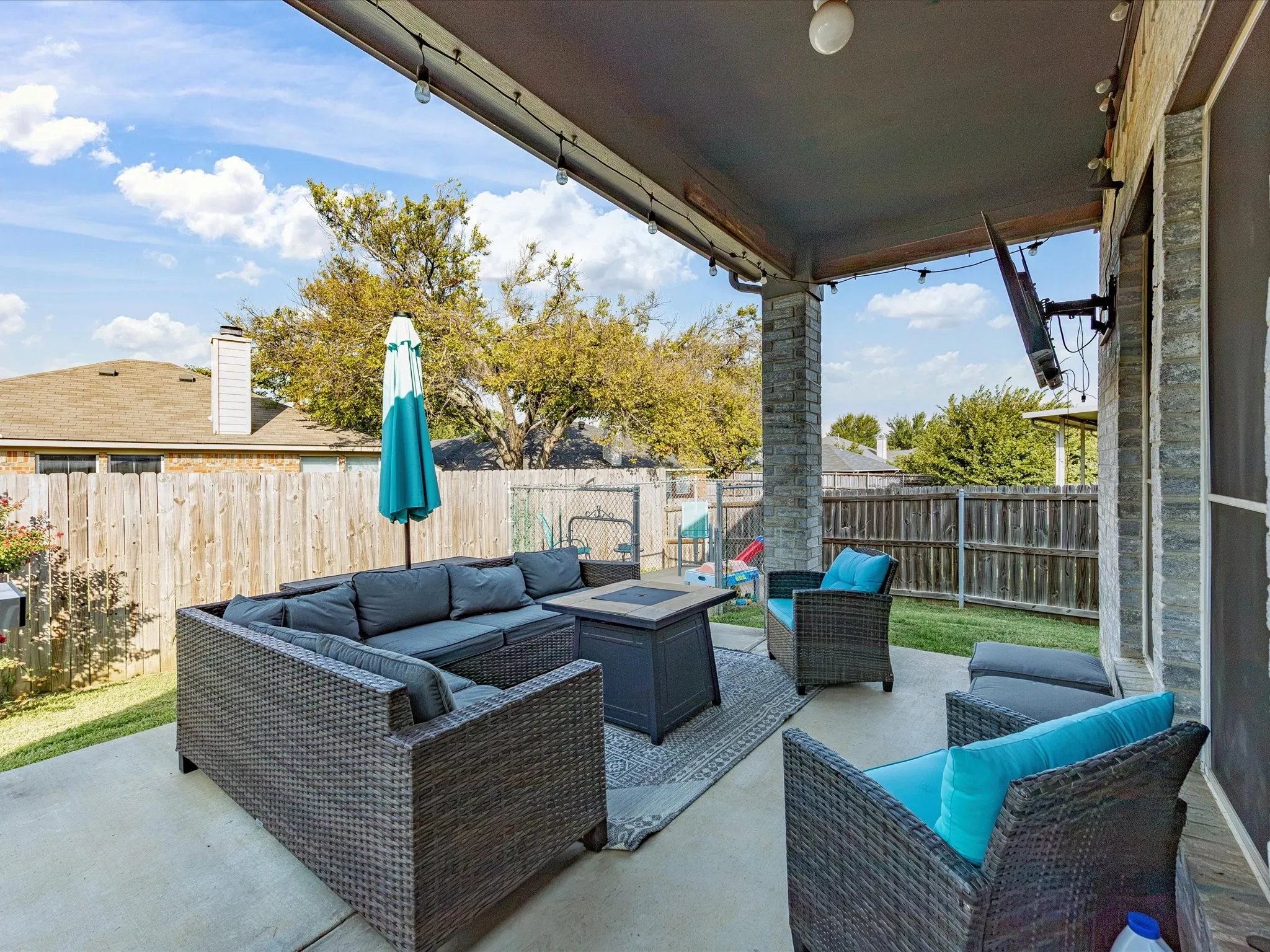 Covered patio featuring concrete flooring, two stone-clad columns, and string lighting