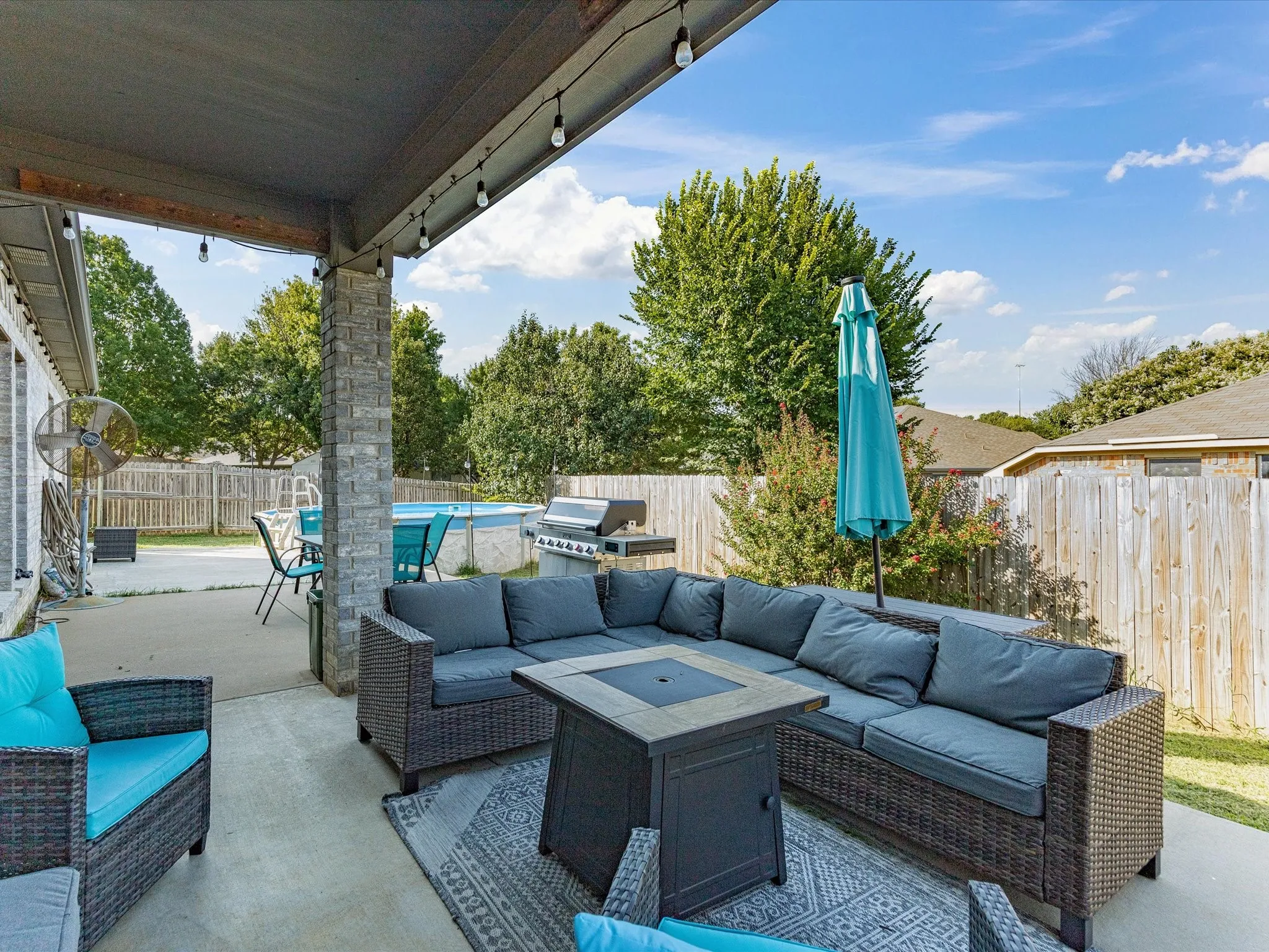 Covered patio with string lighting, stone-clad columns, and a concrete slab