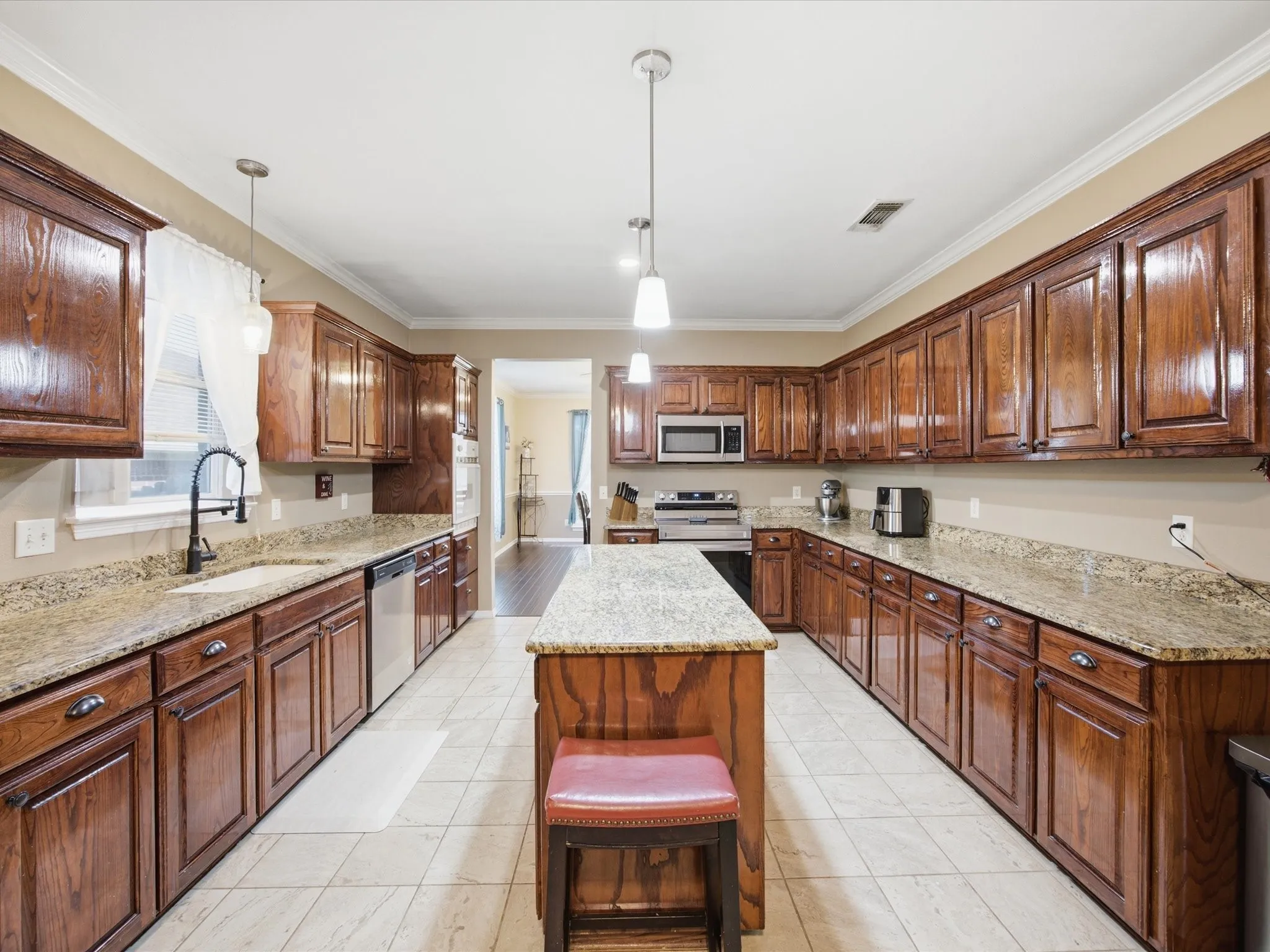 Spacious kitchen featuring extensive wood cabinetry, granite countertops, a central island, stainless steel appliances, and tile flooring