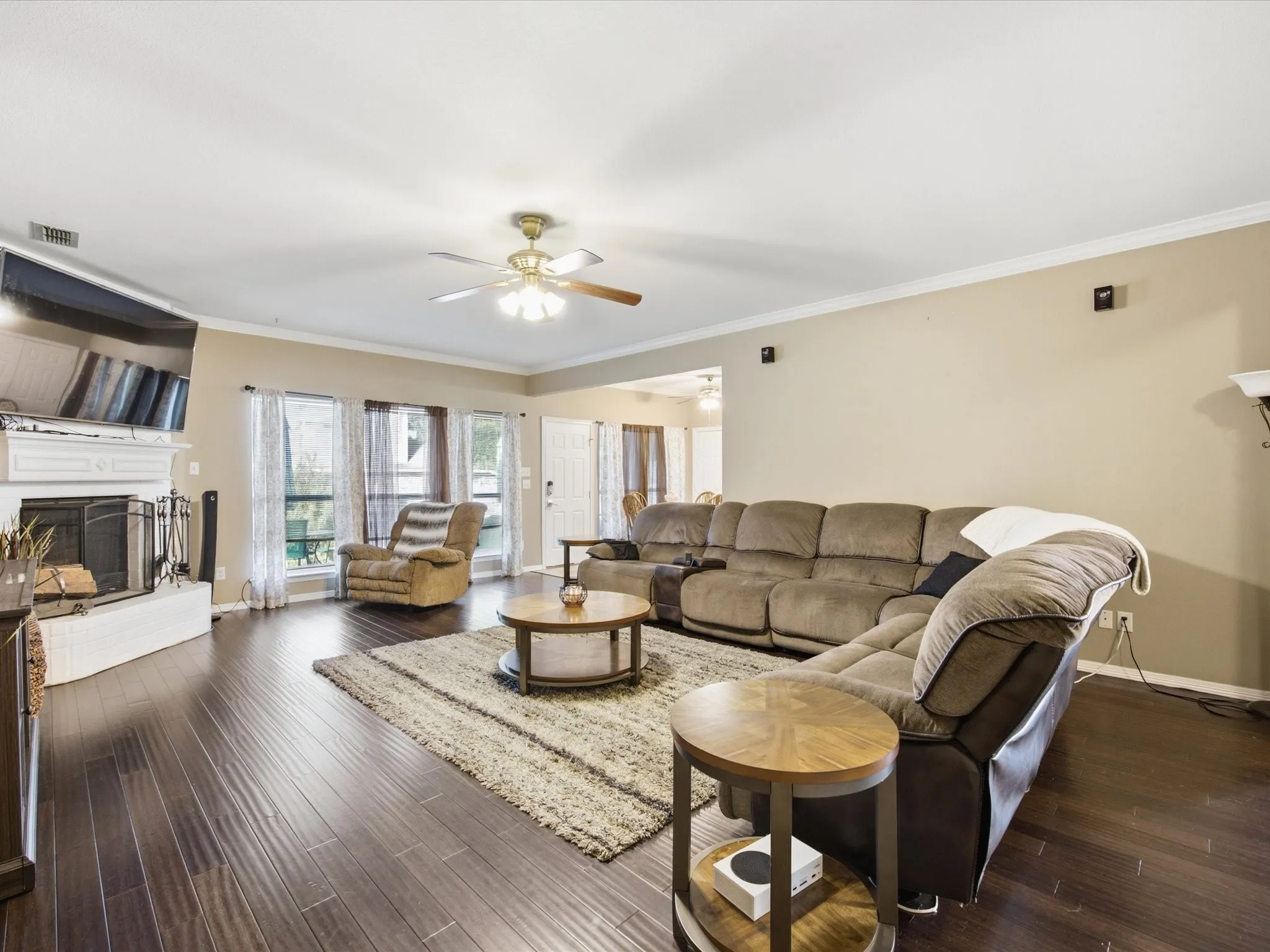 Living room featuring dark wood-finish flooring, a white mantel fireplace, and multiple windows with sheer drapery