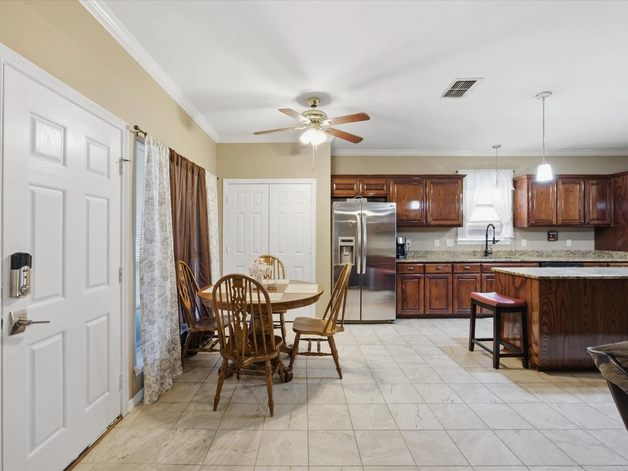 Kitchen and breakfast area featuring tile flooring, wood cabinetry, stone countertops, and stainless steel appliances