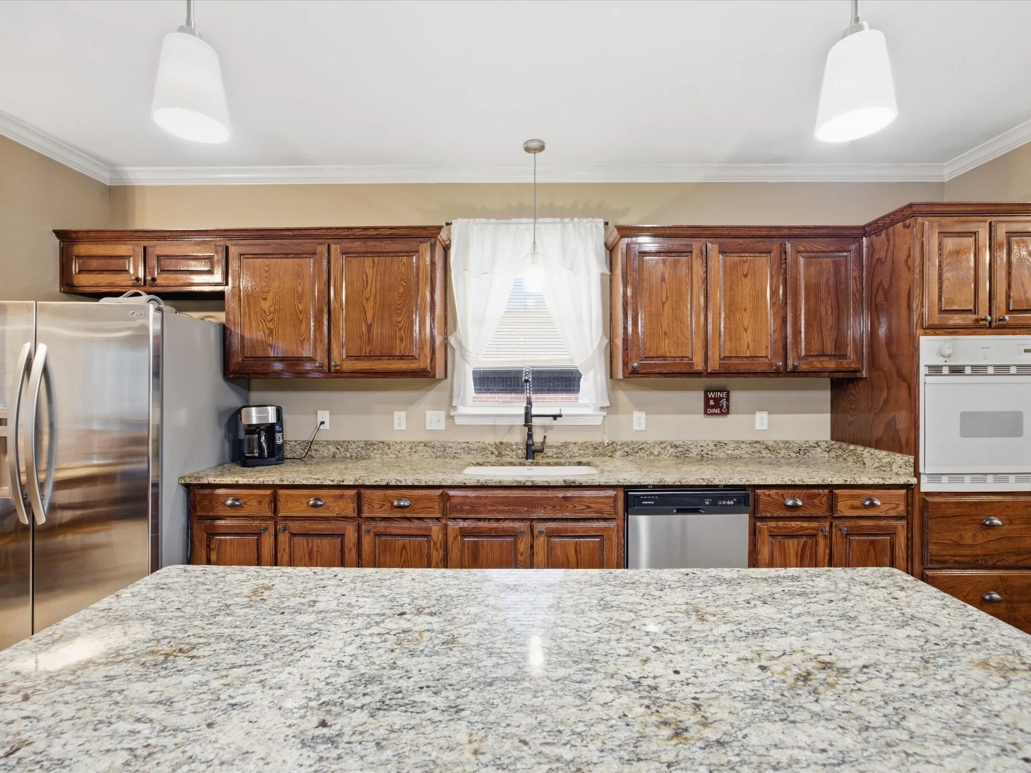 Kitchen featuring a granite-finish island, wood cabinetry, built-in oven, stainless steel dishwasher, and recessed lighting