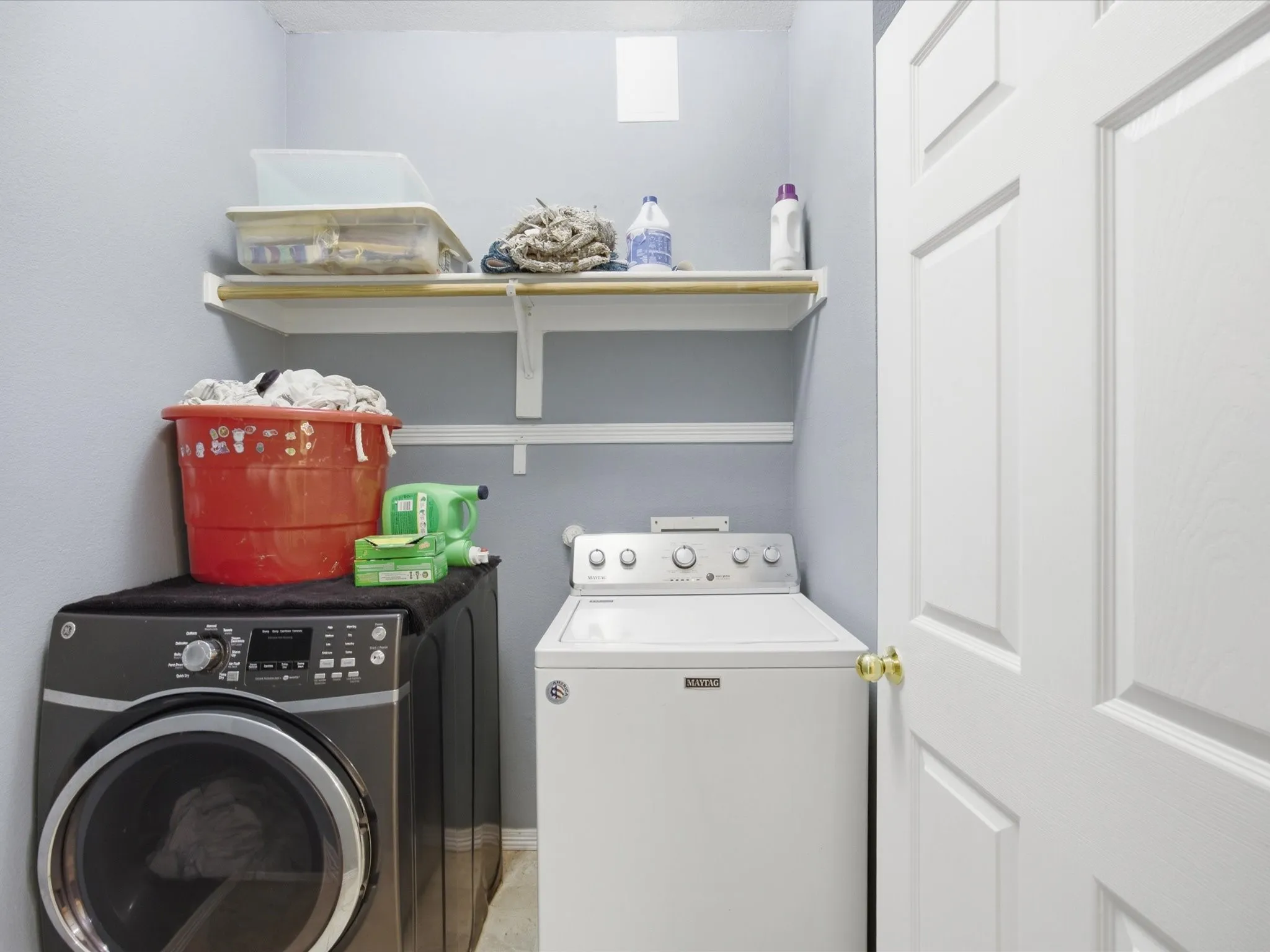 Dedicated laundry space featuring a contemporary washer and dryer, integrated shelving, and a paneled door