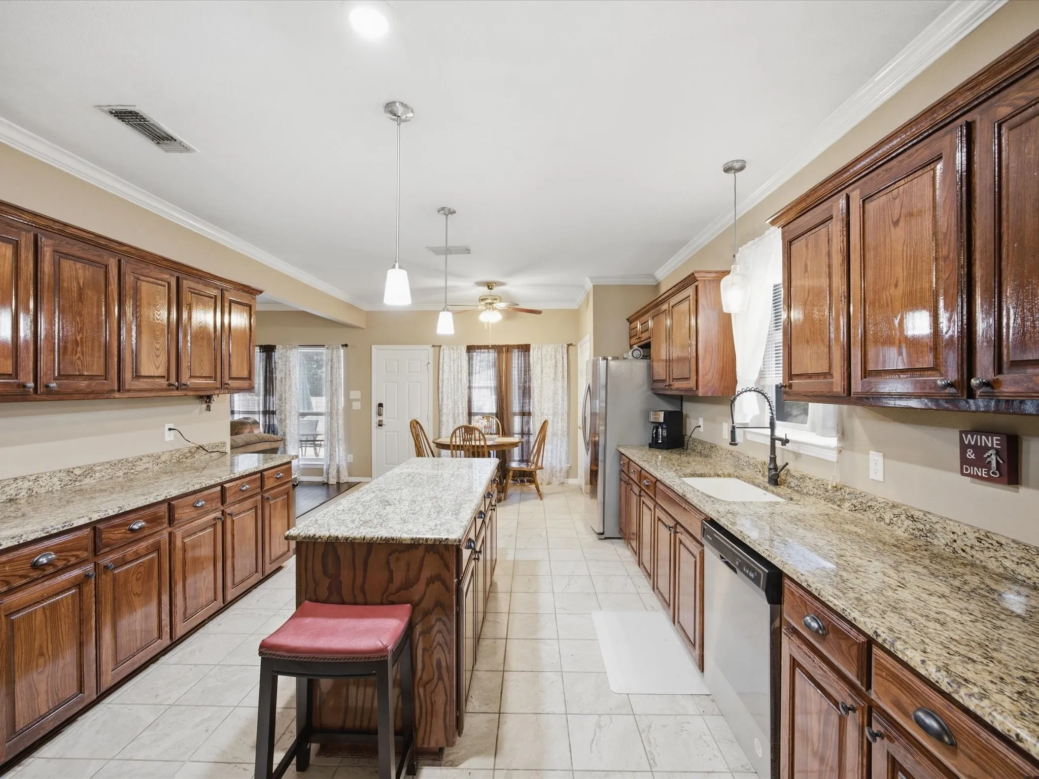 Kitchen featuring wood cabinetry, granite countertops, a central island with seating, stainless steel appliances, and tile flooring