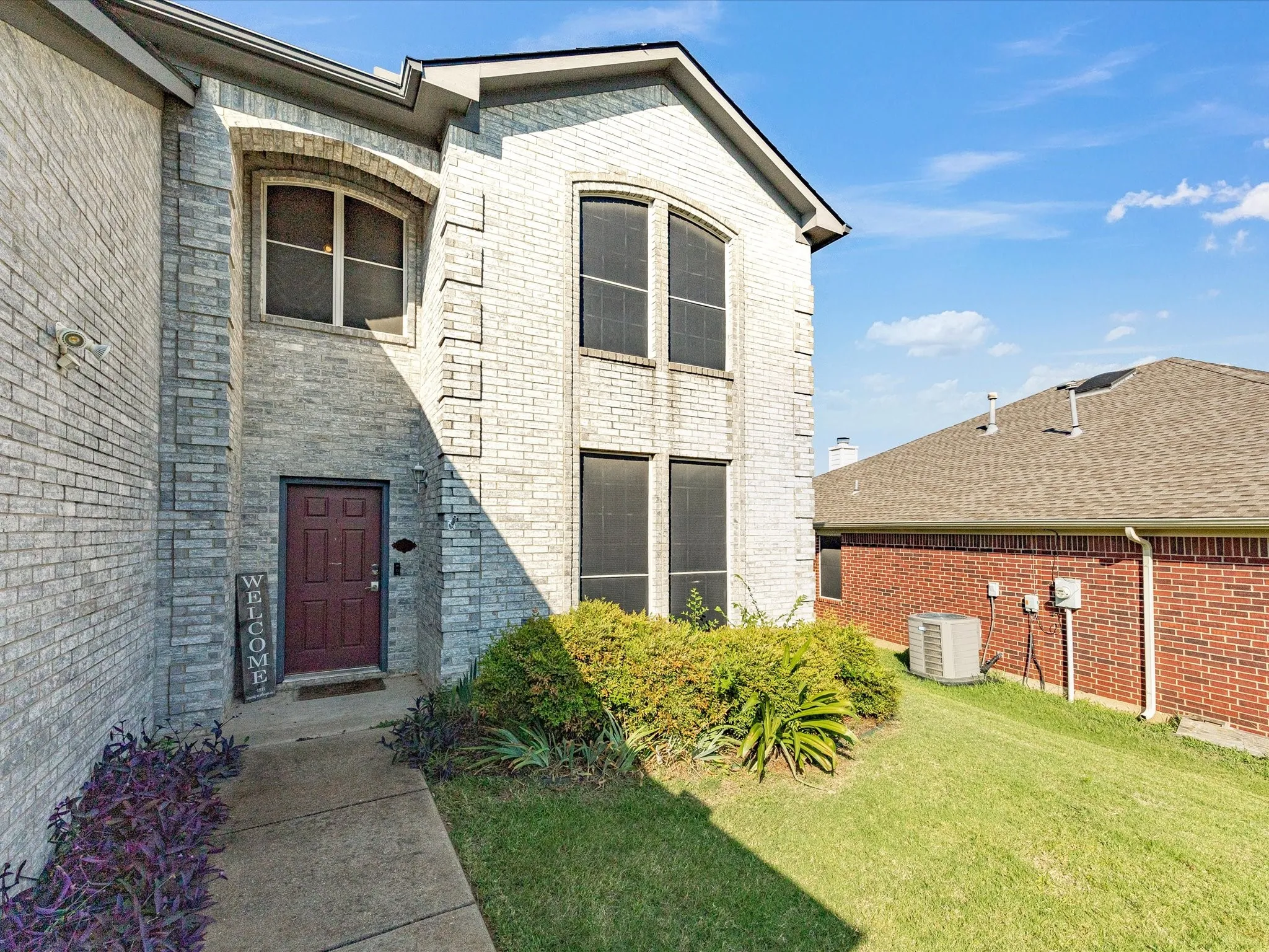 Brick exterior with decorative stone accents, a dark-paneled entry door, arched transom window, and a concrete walkway