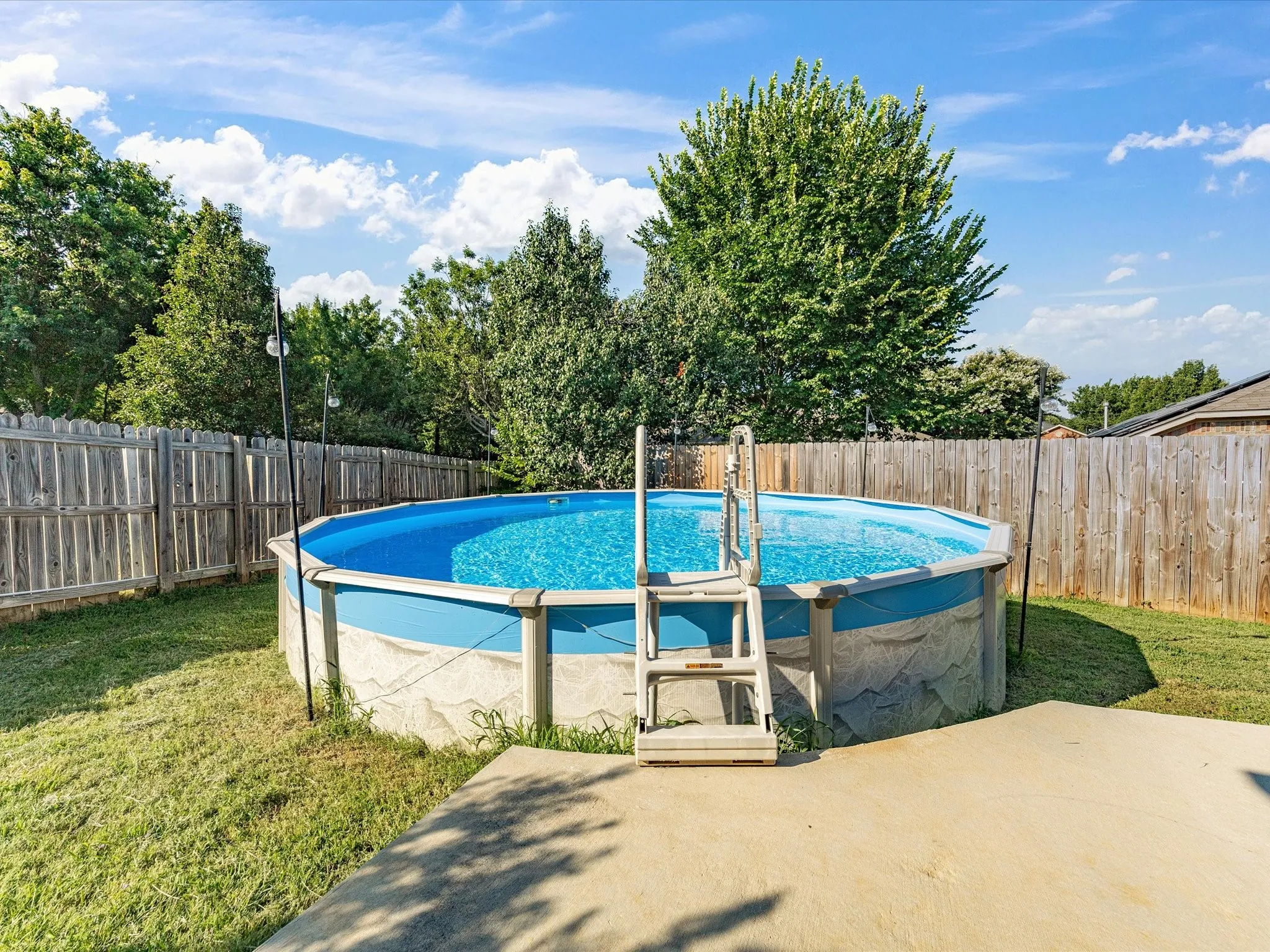 Private backyard featuring an above-ground pool, wood privacy fencing, and a concrete patio area