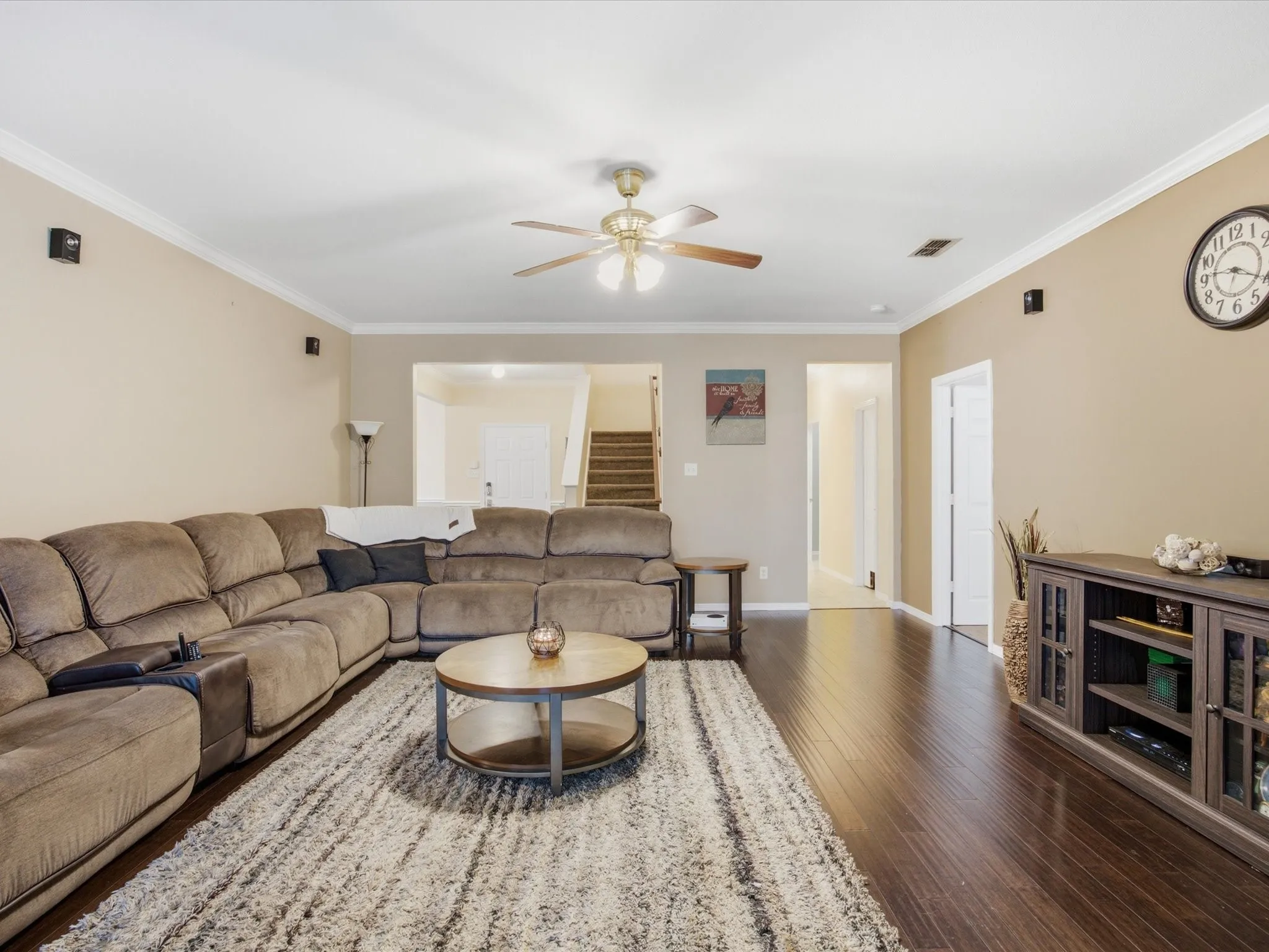 Spacious living area featuring dark wood-finish flooring, crown molding, and a ceiling fan