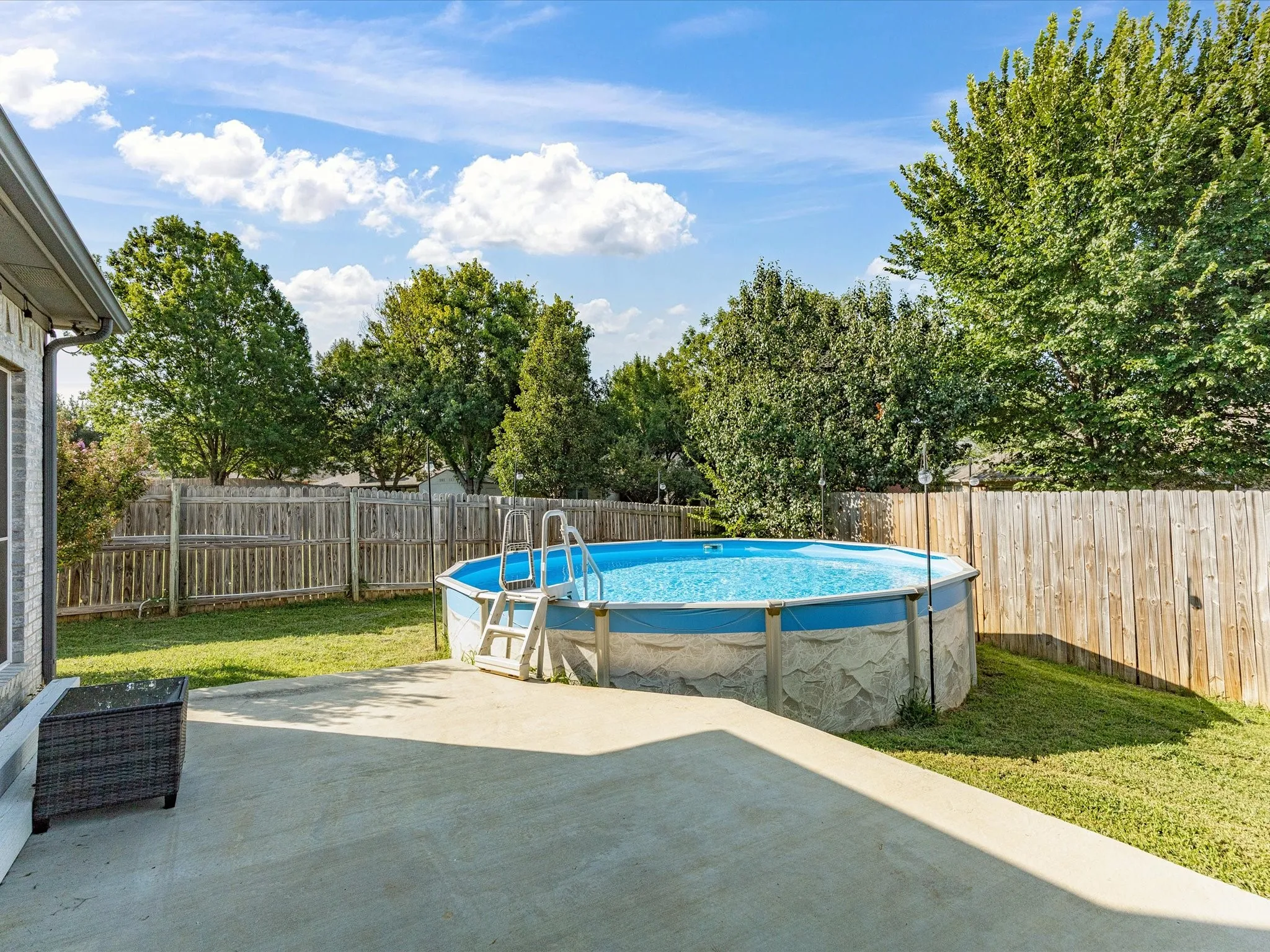 Expansive backyard featuring a large above-ground pool with ladder, concrete patio, and mature trees