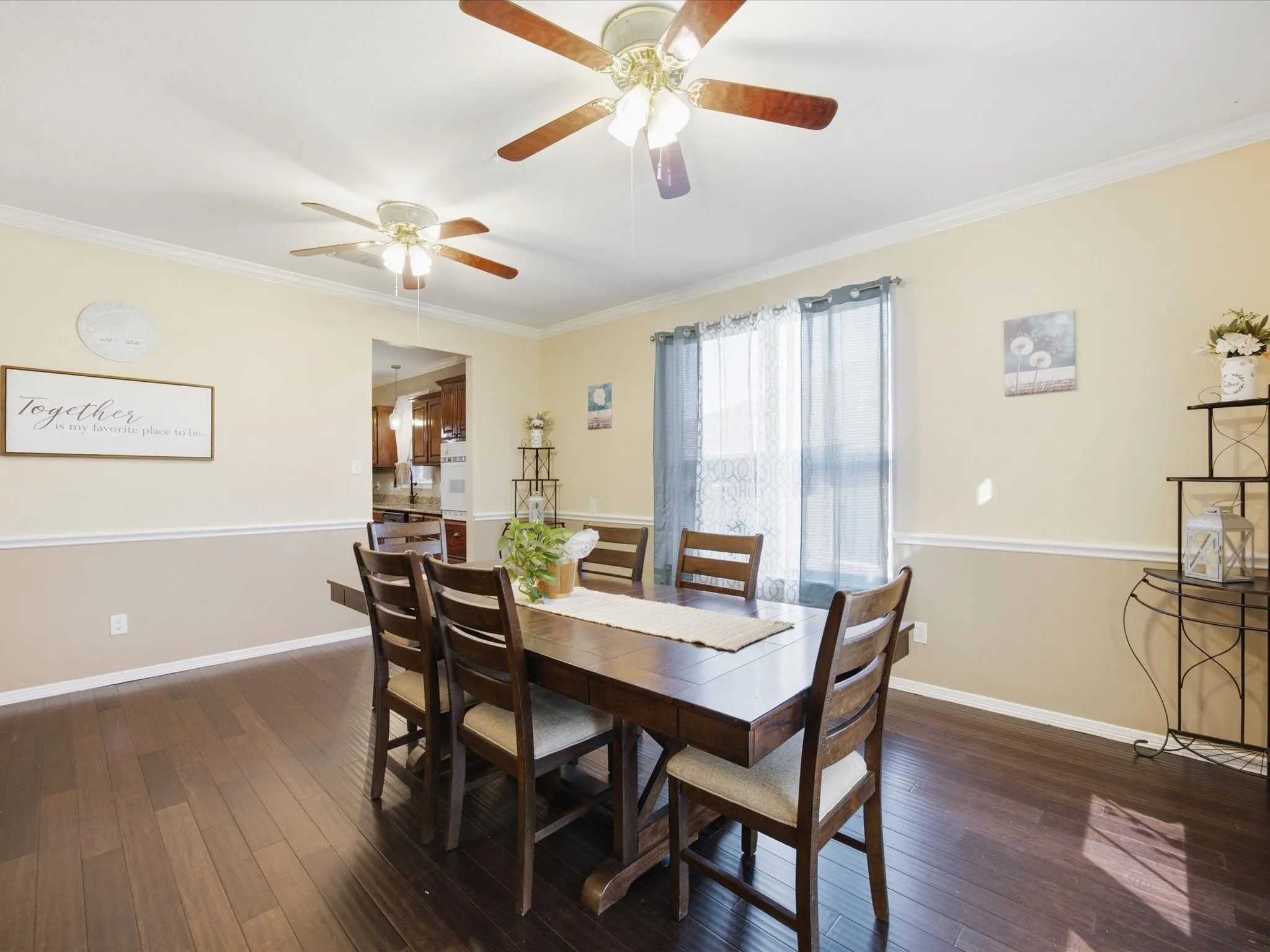 Dining area featuring wood-finish flooring, a two-tone wall treatment, crown molding, and two ceiling fans