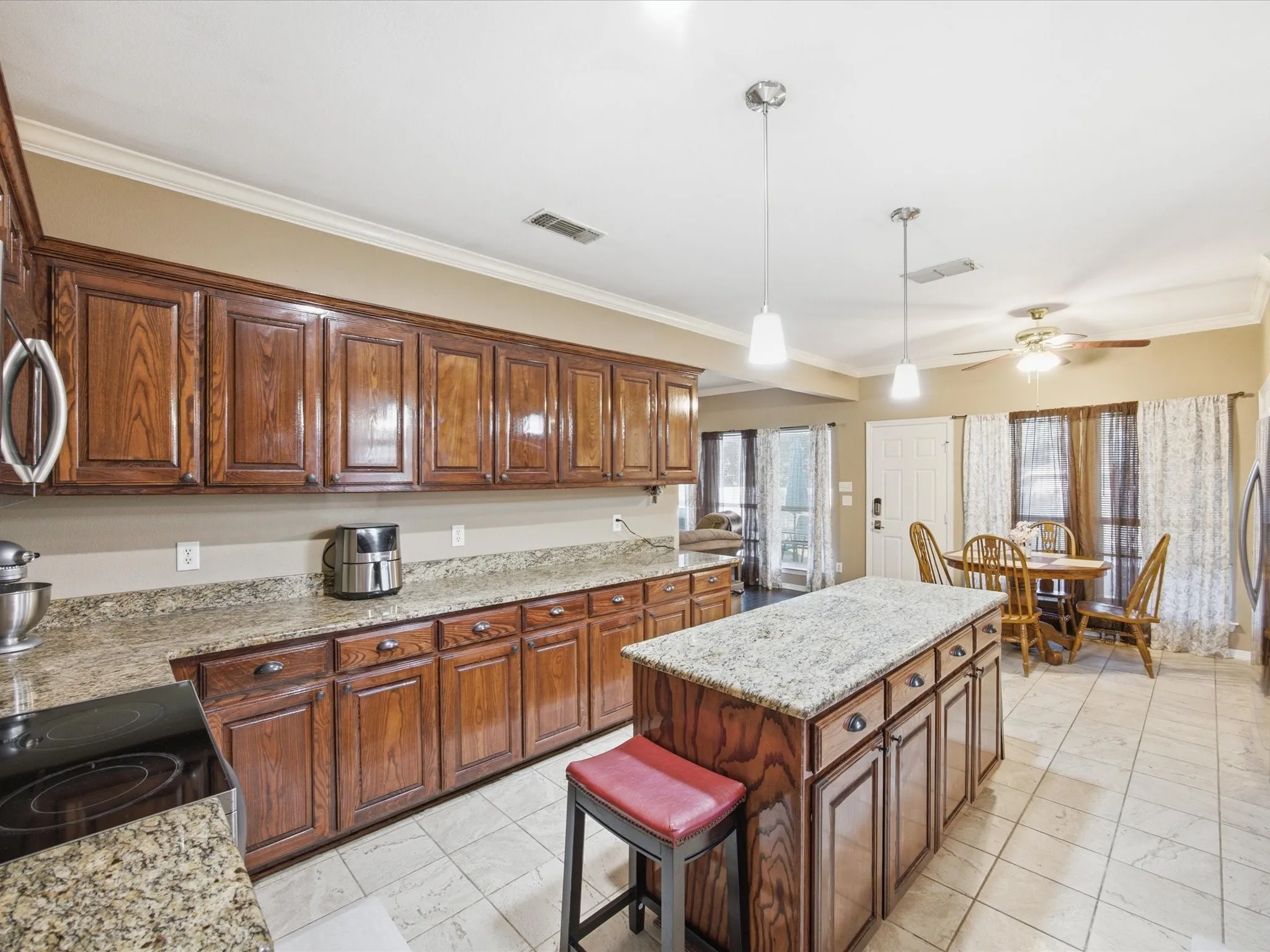 Kitchen featuring wood-finish cabinetry, light-toned countertops, a center island with pendant lighting, and tile flooring