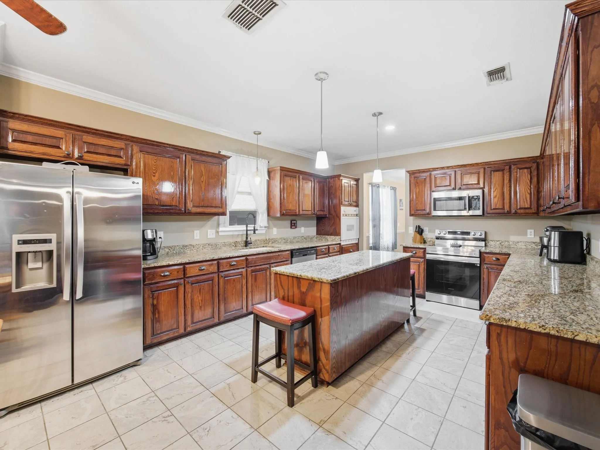 Kitchen featuring a central island, granite countertops, wood cabinetry, tile flooring, and stainless steel appliances
