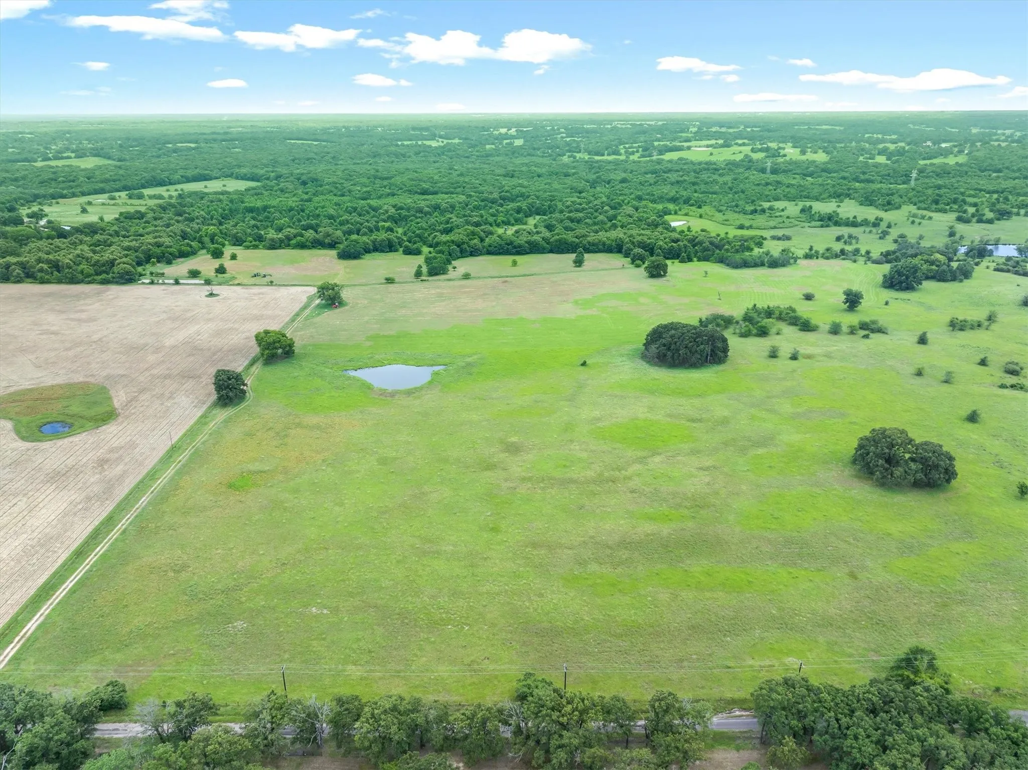 Expansive open land featuring diverse topography, including a large cultivated field, a verdant pasture, and areas of mature trees