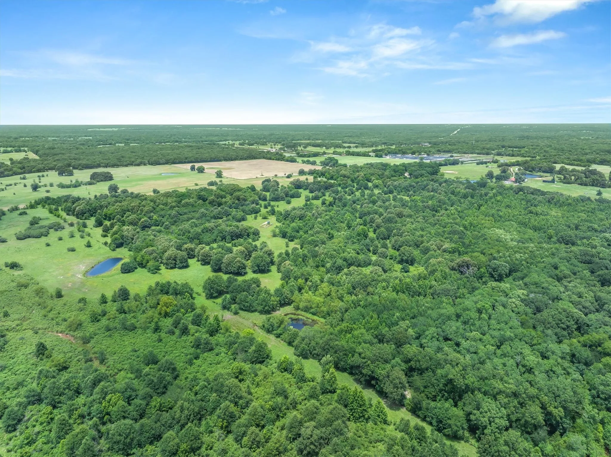 Expansive rural landscape featuring dense woodlands, open fields, and multiple visible ponds