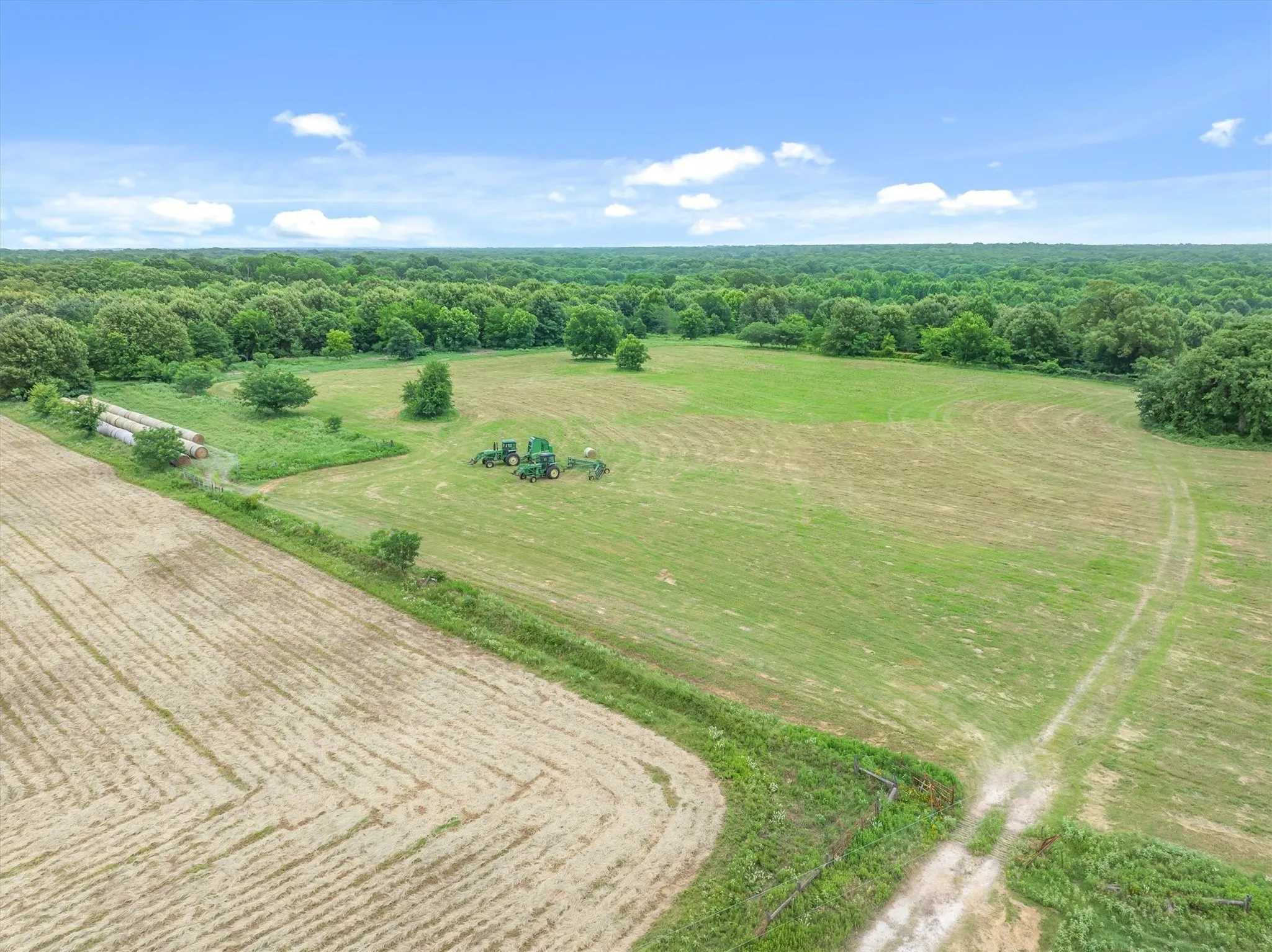 Expansive agricultural property featuring a cultivated field, verdant pastures, and mature tree lines
