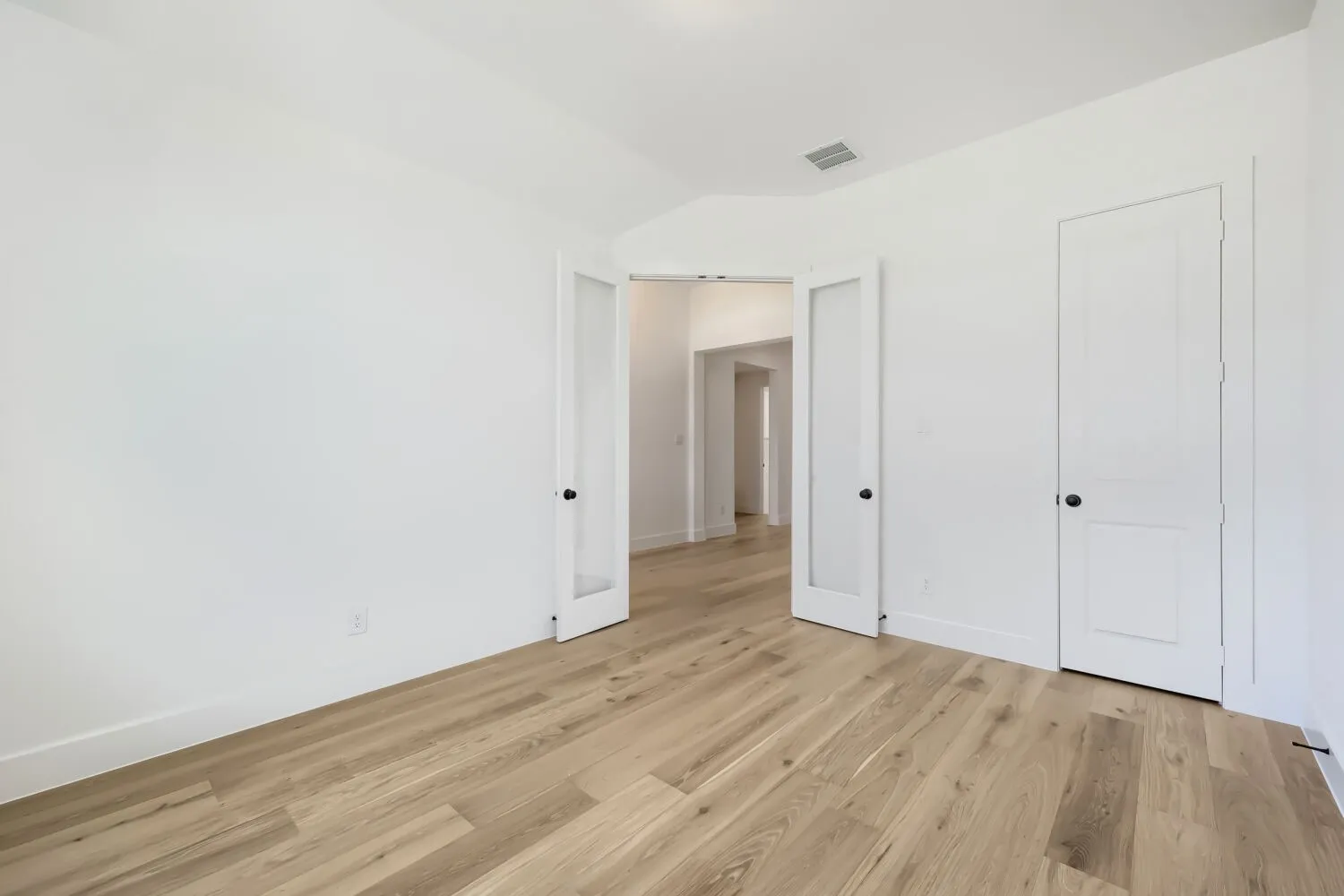 Spacious room featuring light wood-finish flooring, white walls, and a recessed ceiling