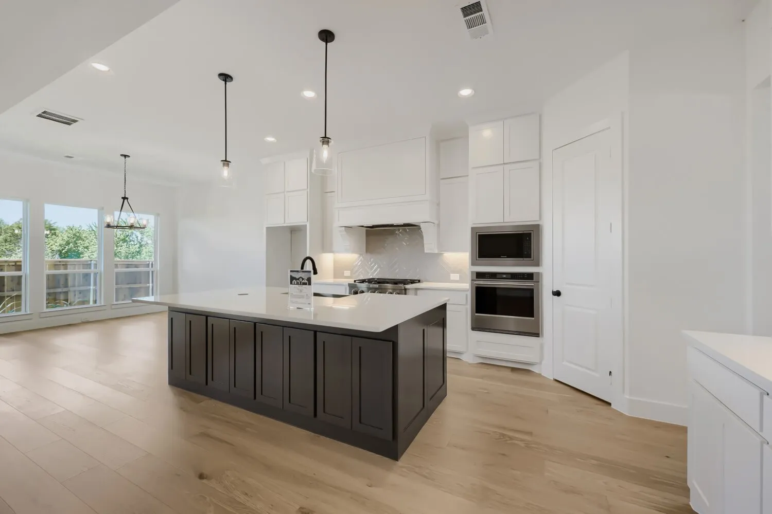 Modern kitchen featuring a large island with dark cabinetry and a light-toned countertop, white upper cabinetry, and stainless steel built-in appliances