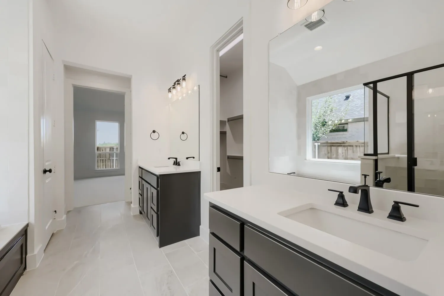 Bathroom featuring dual vanities with dark cabinetry and light countertops, large wall-mounted mirrors, and matte black fixtures