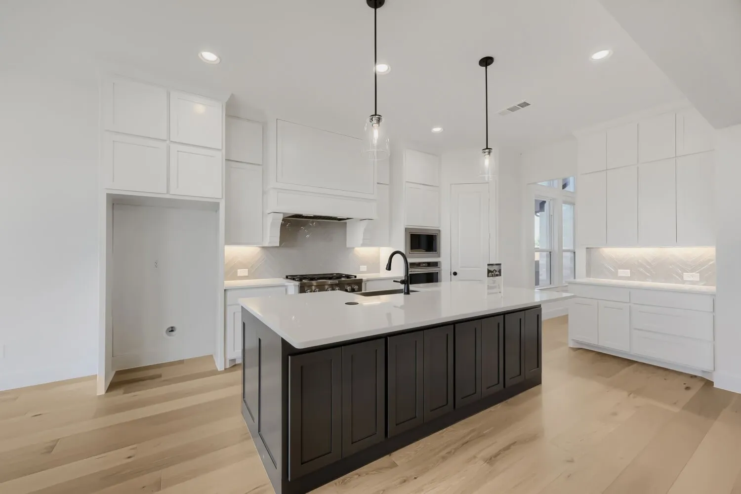 Spacious kitchen featuring a dark-toned island with a light countertop, white perimeter cabinetry, stainless steel appliances, and wood-finish flooring