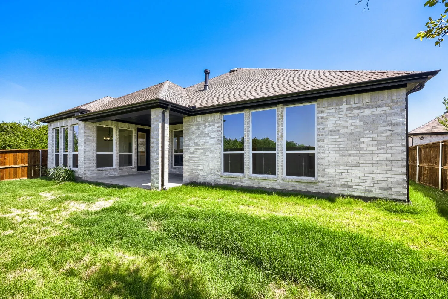 Contemporary light brick exterior featuring multiple large windows, a covered patio, and a shingled roof with dark gutters