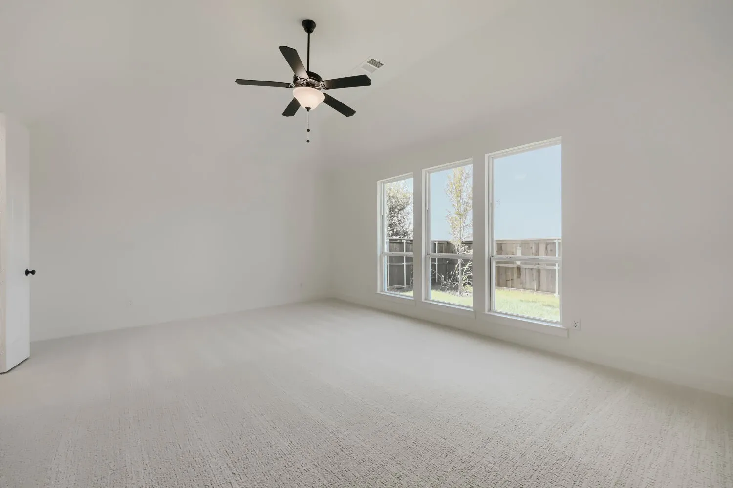 Spacious room featuring light-colored carpeting, white walls, and a ceiling fan with integrated lighting