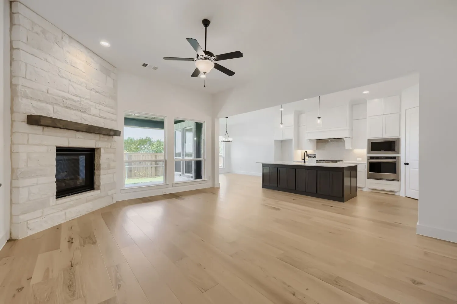 Open-concept living space featuring a stone-clad fireplace with a wood mantel, wood-finish flooring, and a vaulted ceiling with a ceiling fan