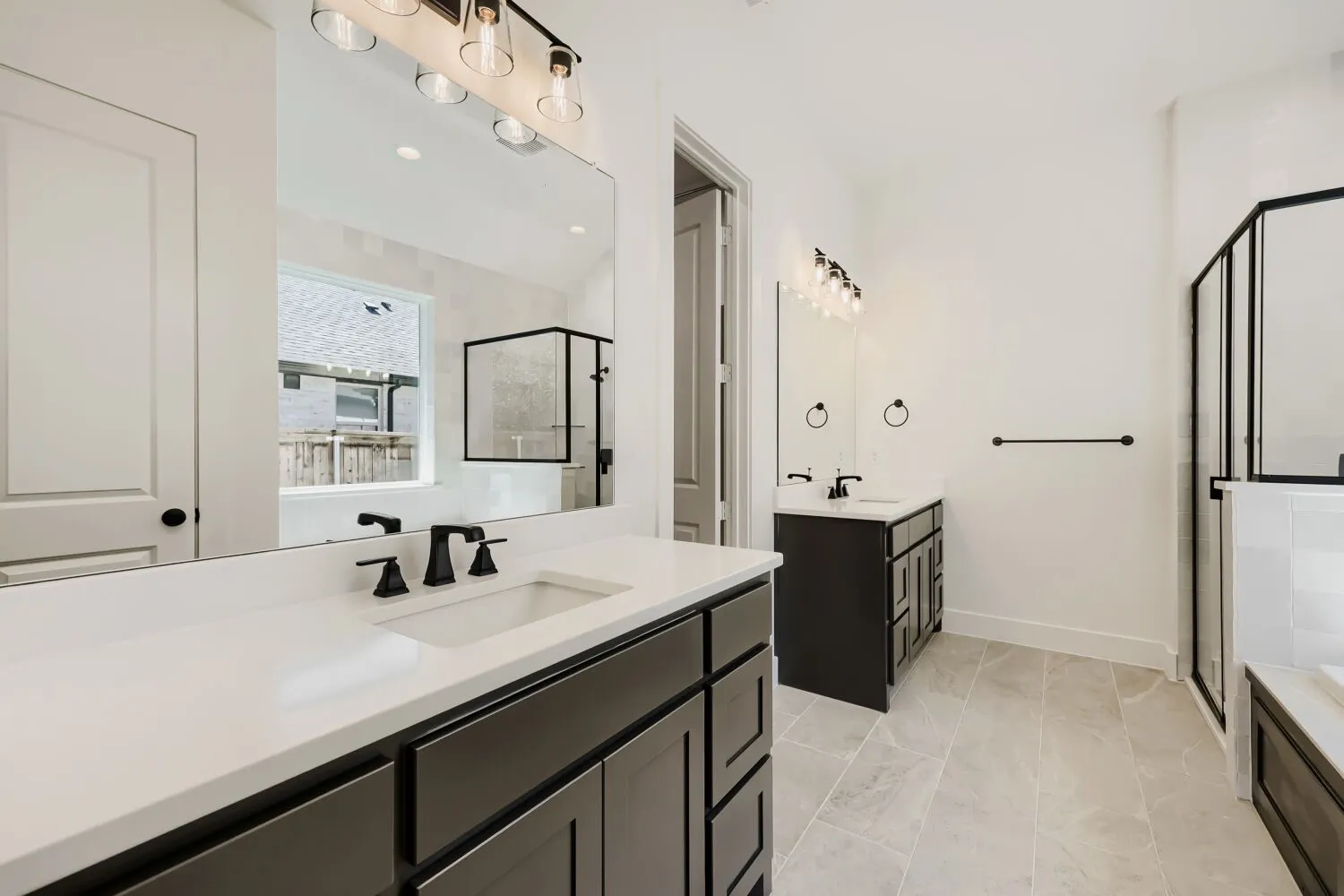 Dual vanity bathroom featuring light-toned tile flooring, black cabinetry, white countertops, and matte black fixtures