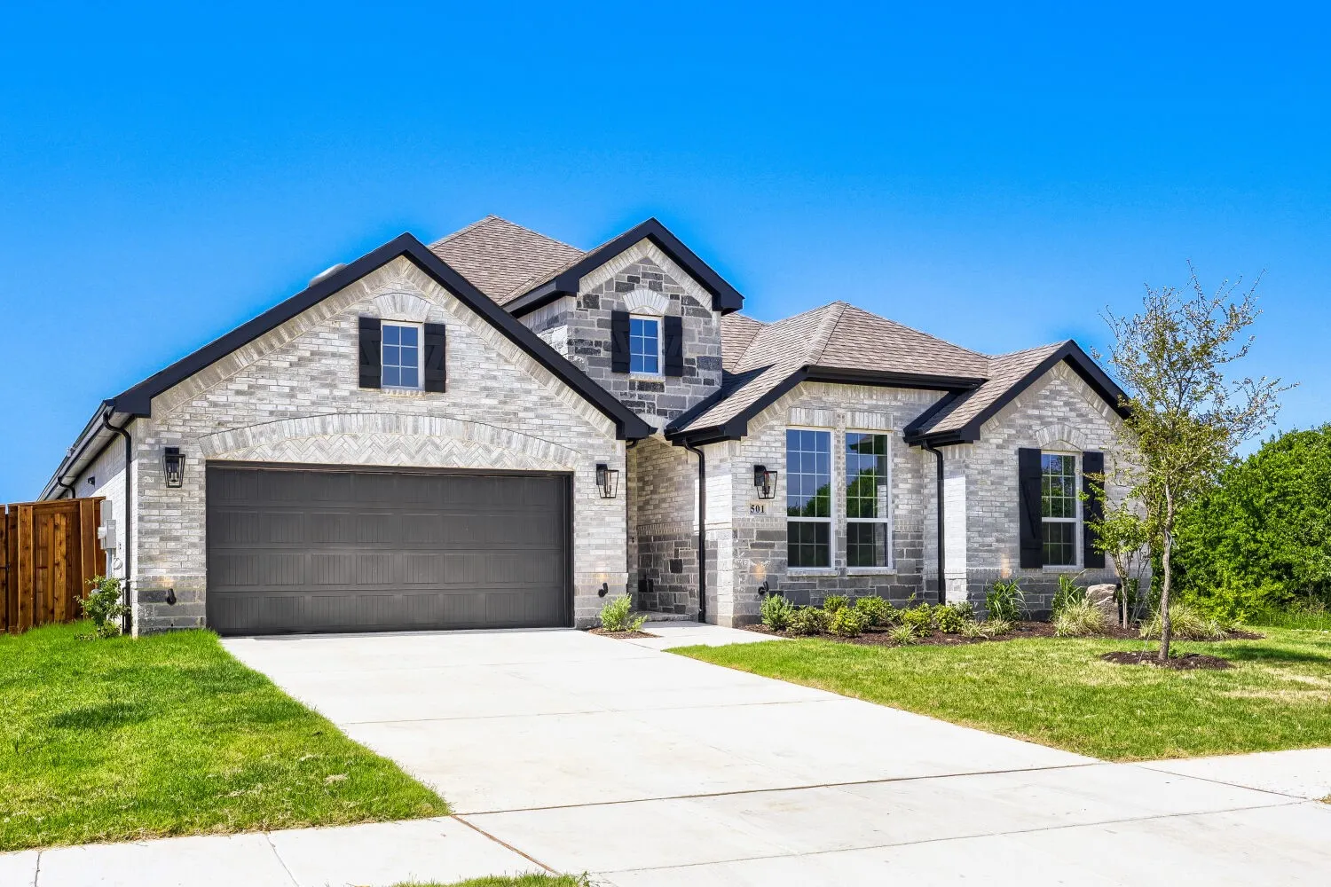 Stone and brick veneer exterior featuring a two-car garage, multiple gables, dark trim, and a prominent front entrance with large windows
