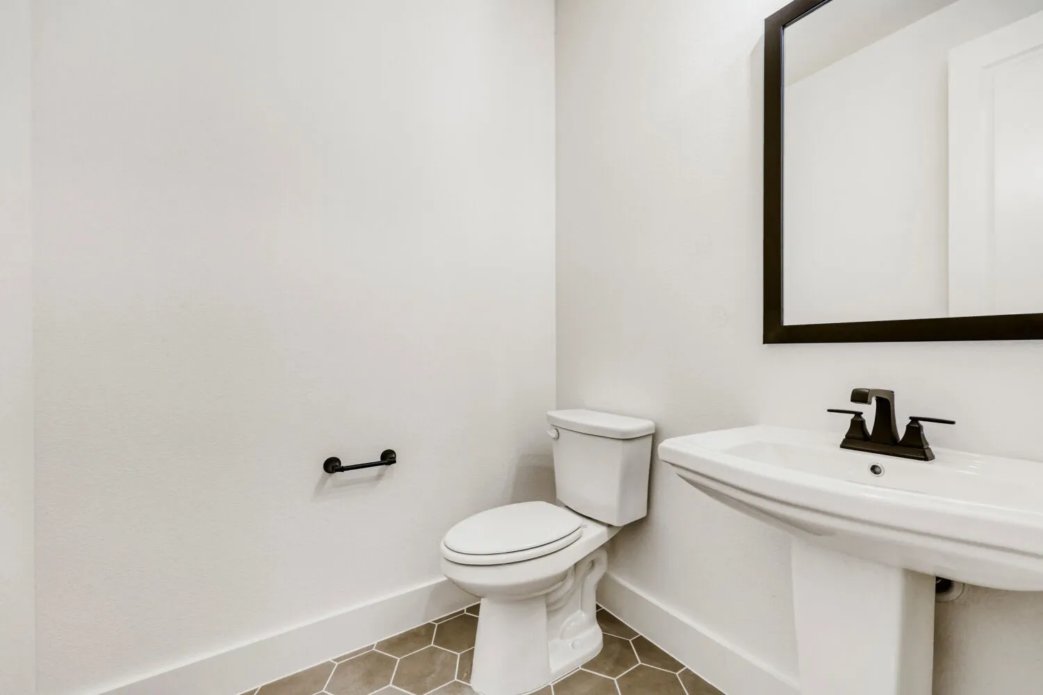 Pedestal sink with black faucet, framed mirror, and hexagonal floor tiling