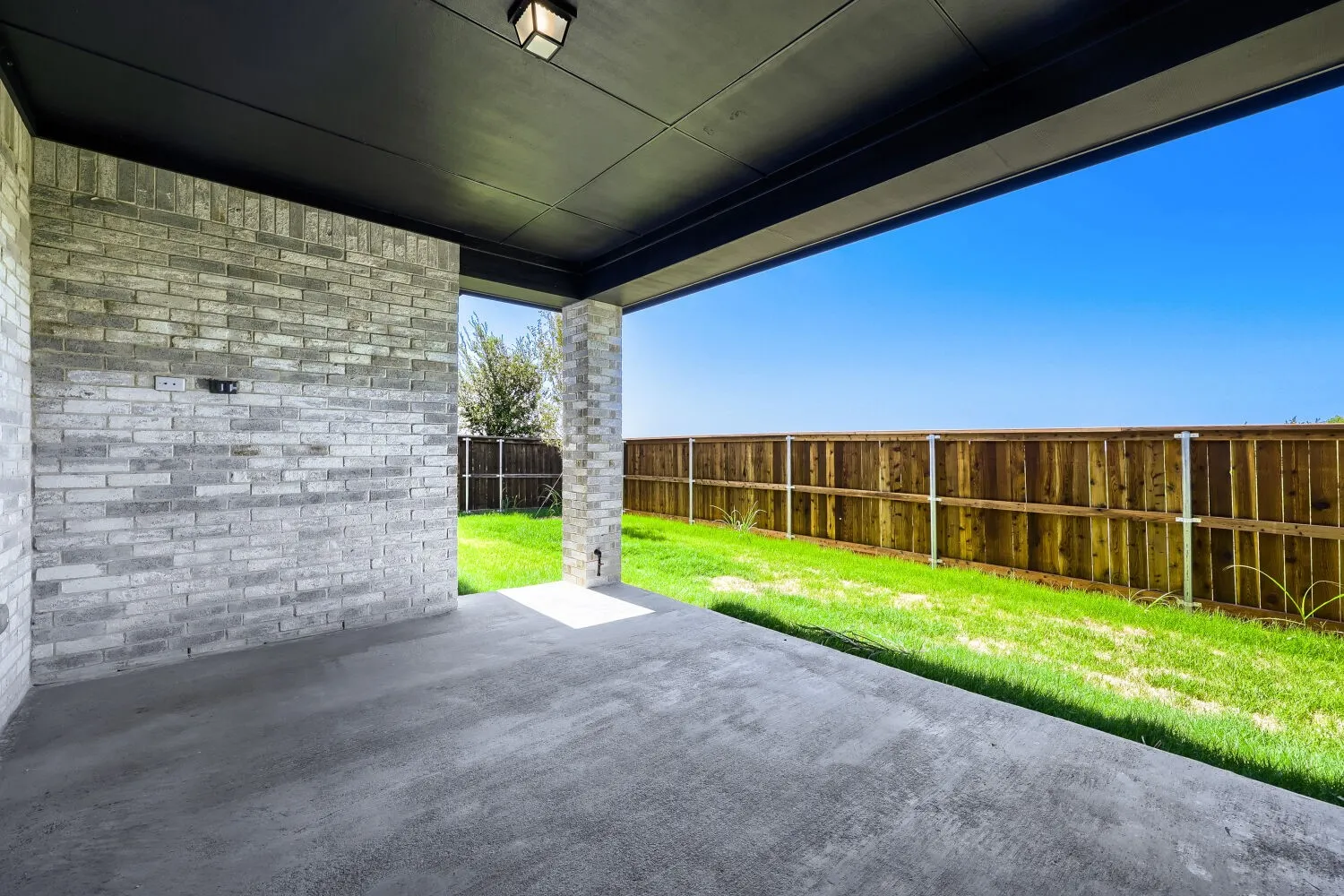 Covered patio with a concrete slab, gray brick accent wall, and a dark wood soffit ceiling with recessed lighting