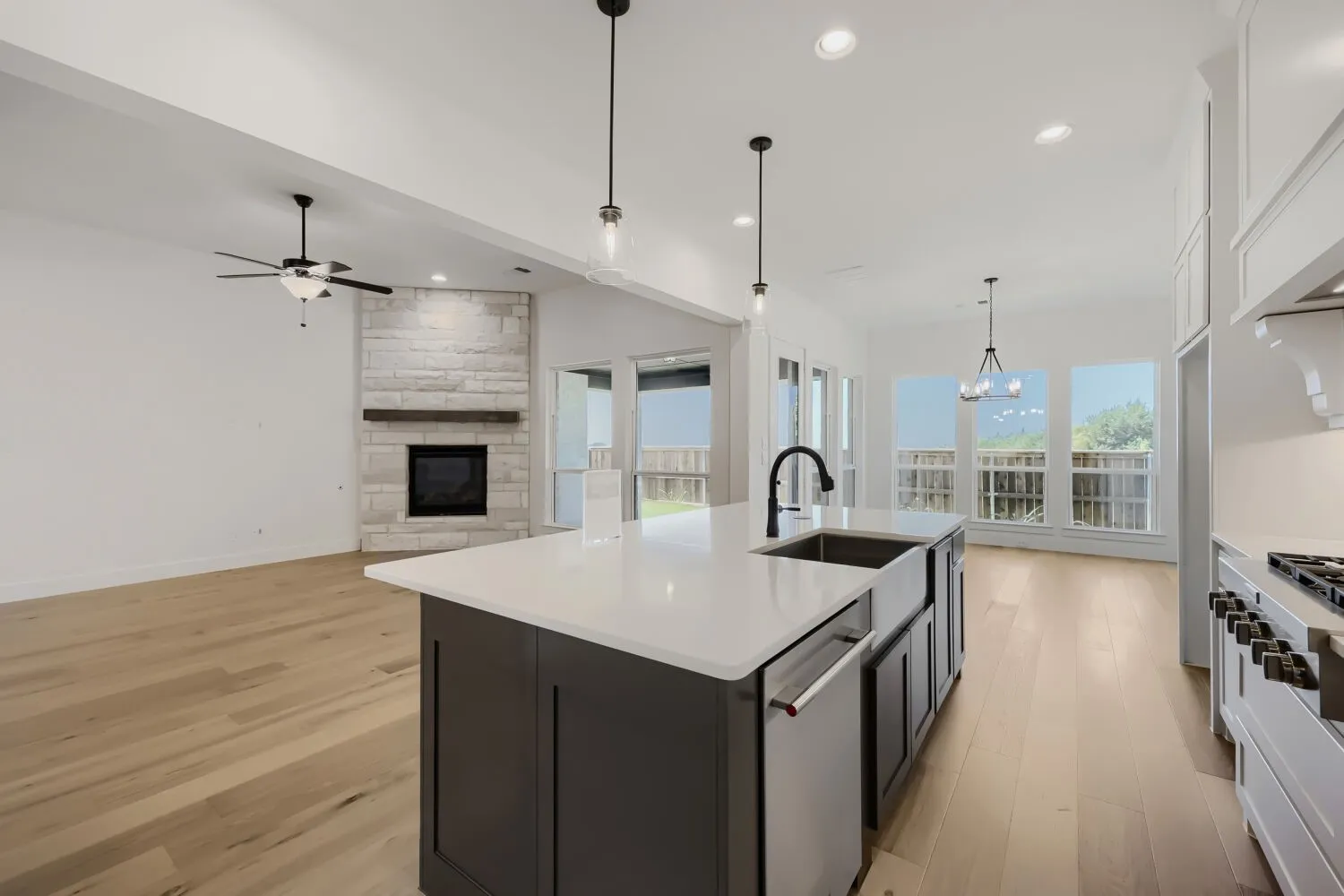 Open-concept living space featuring a central kitchen island with a farmhouse sink, stainless steel appliances, and wood-finish flooring