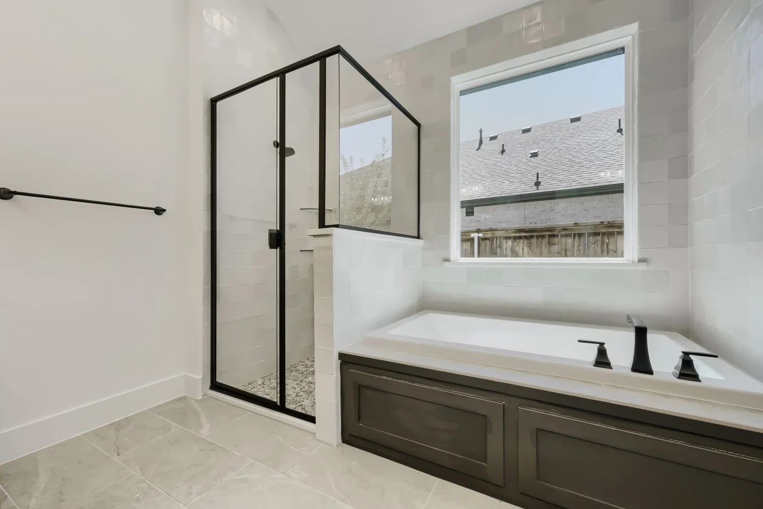 Contemporary bathroom featuring a built-in tub with matte black fixtures, a separate shower with black-framed glass enclosure and pebble floor, light-toned wall tile, and large format floor tiles