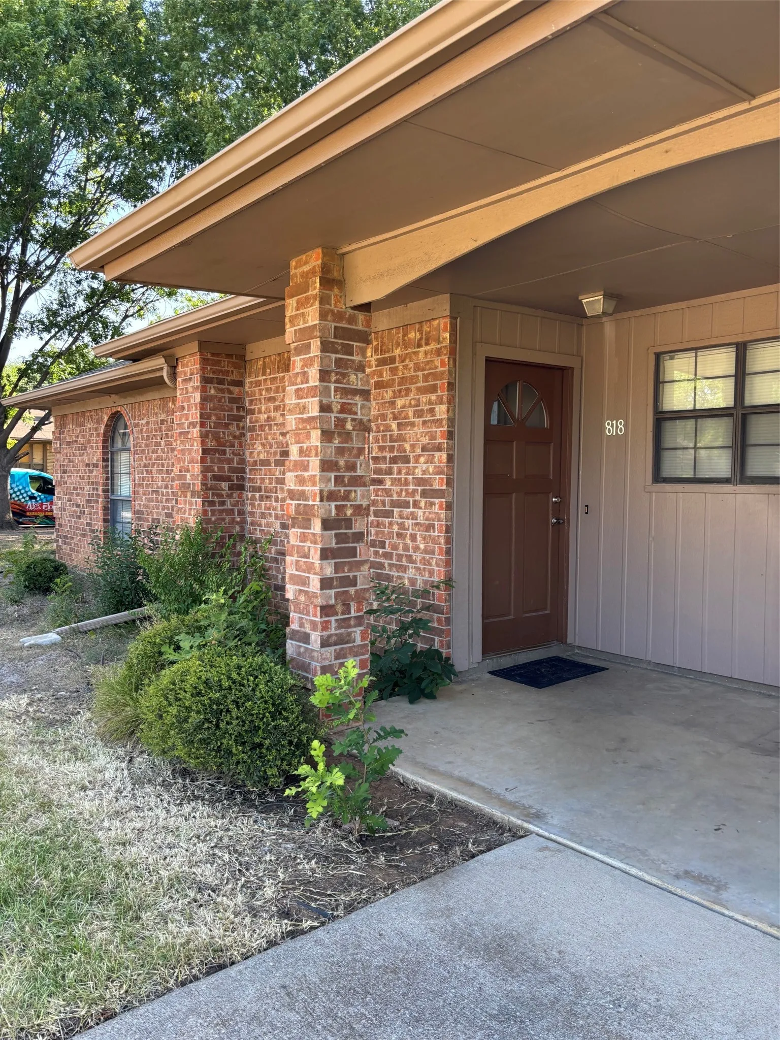 Brick exterior with a covered entry, featuring a brown paneled door with a decorative glass insert