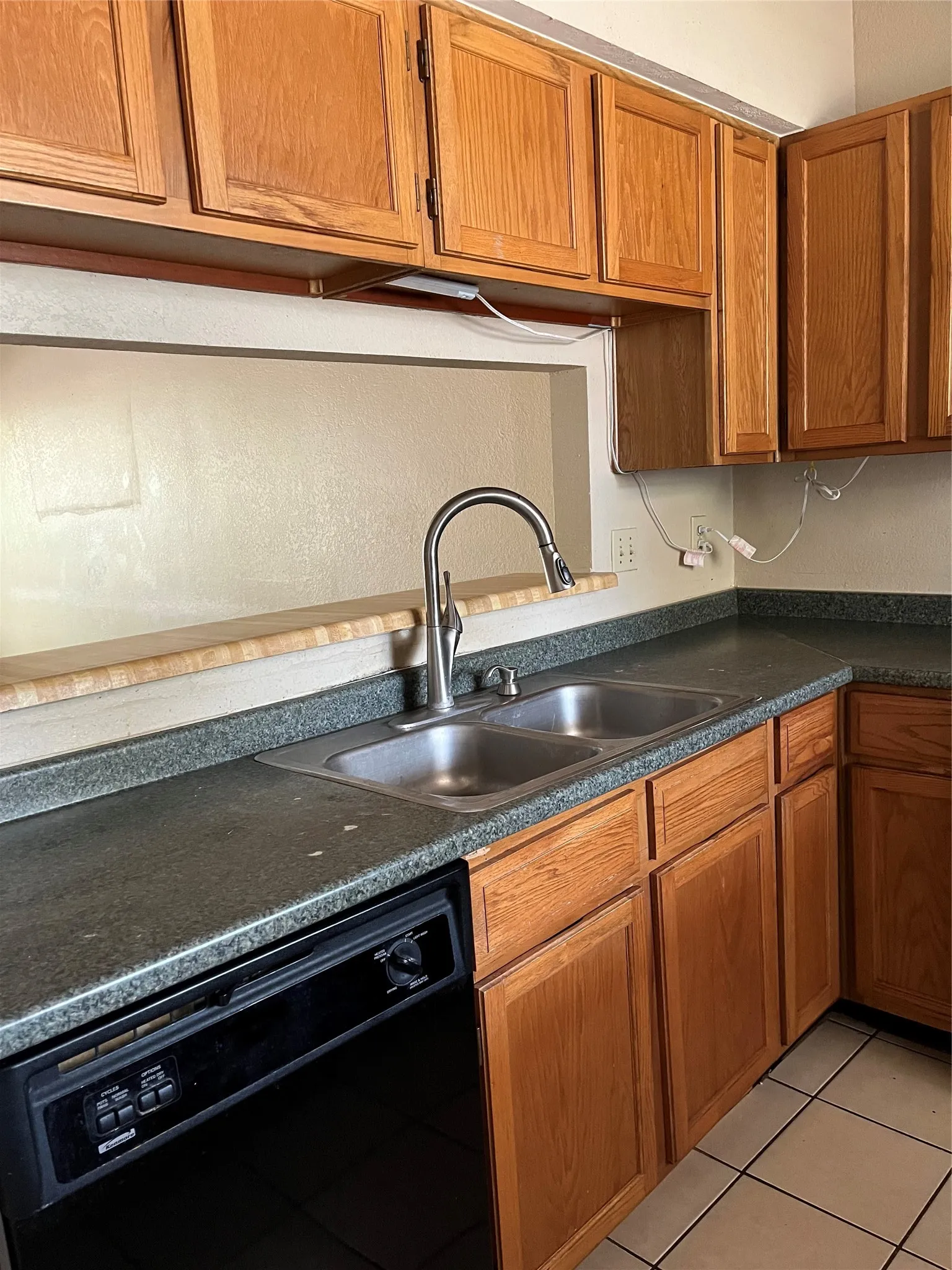 Kitchen featuring wood-finish cabinetry, a double basin stainless steel sink with a gooseneck faucet, dark speckled countertops, and a built-in black dishwasher