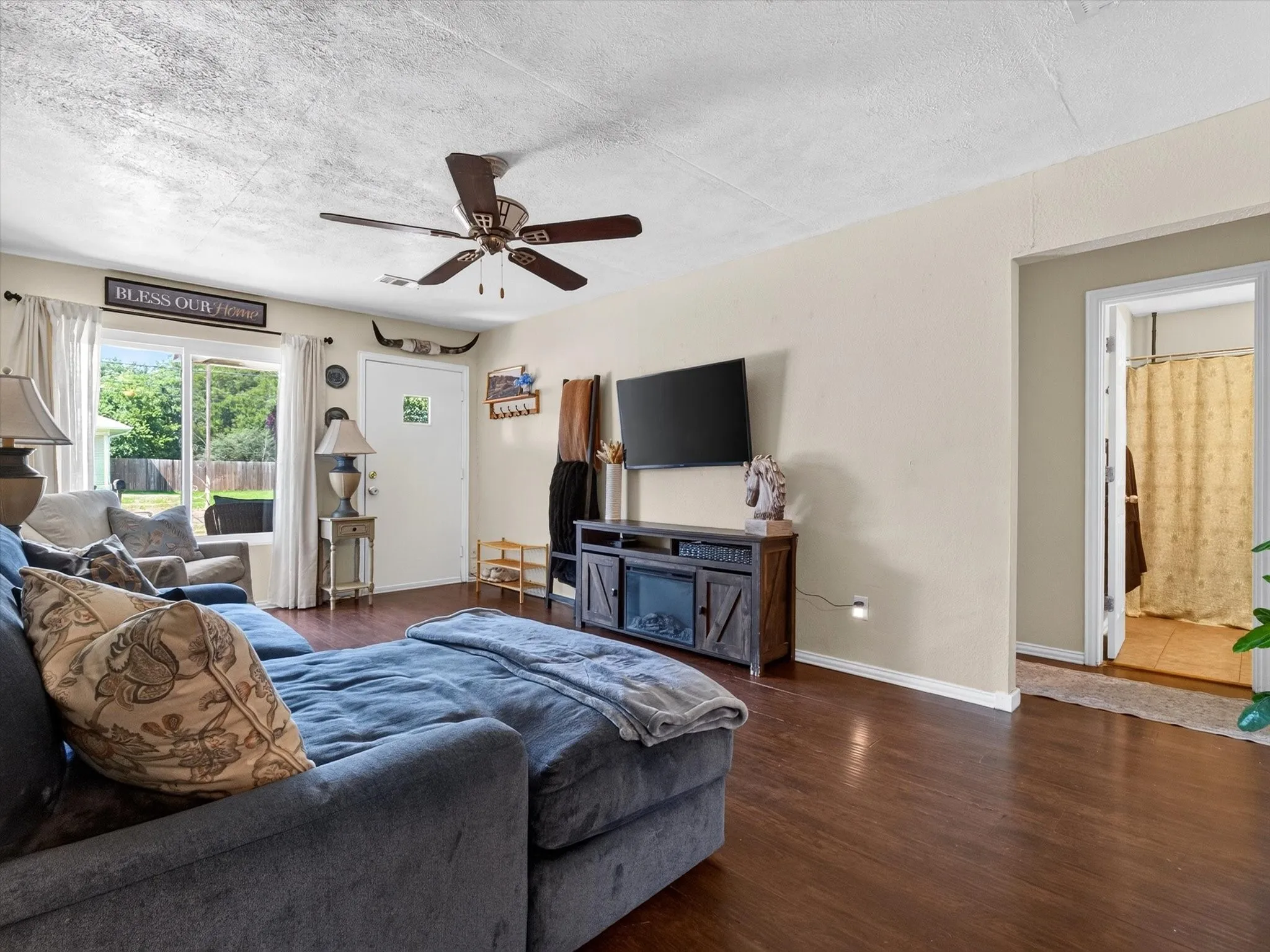 Living area featuring wood-finish flooring, a ceiling fan with light fixture, and a window overlooking the backyard